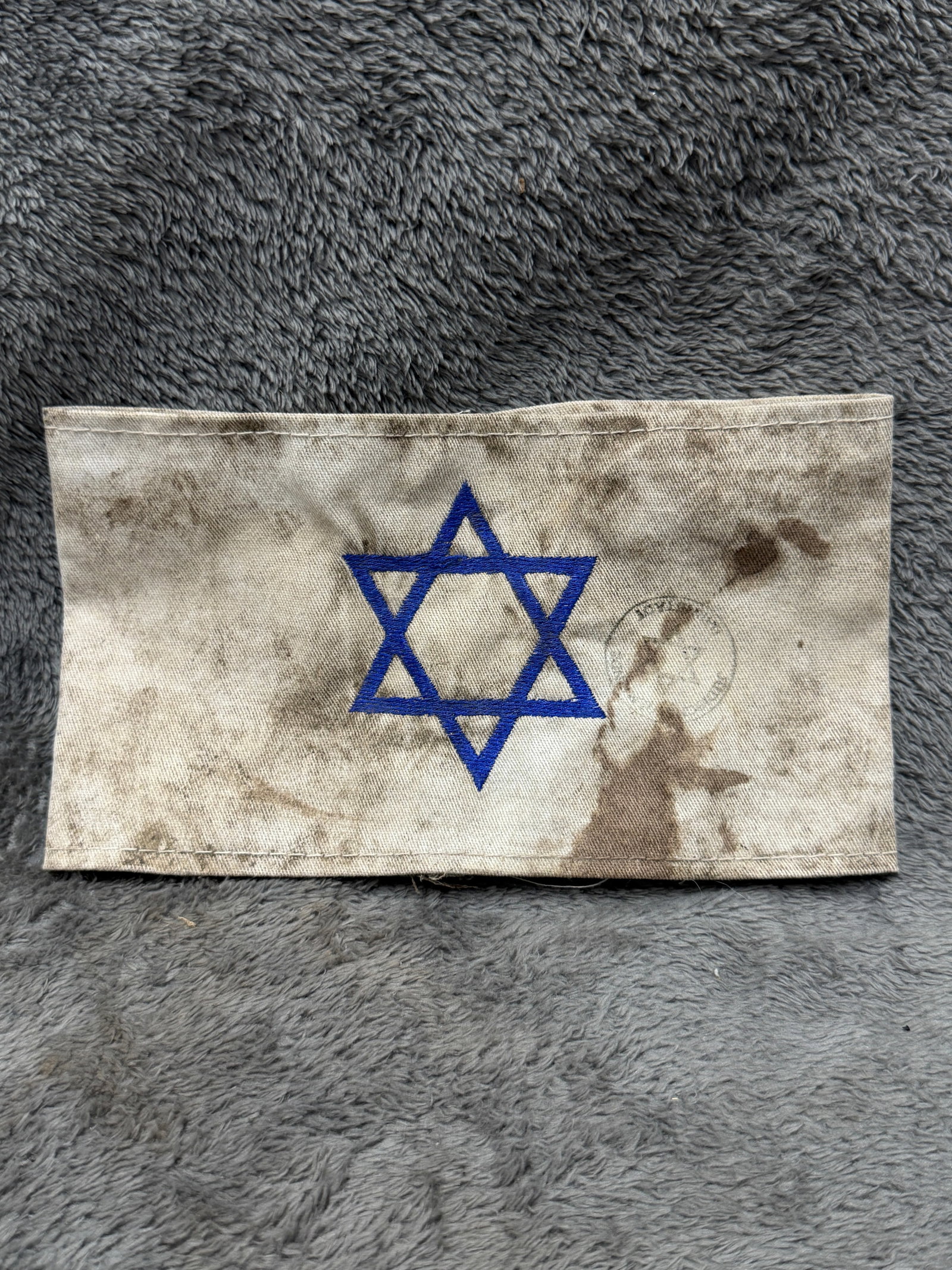 WWII Jewish Prisoner Star of David Concentration Camp Identification Armband: A WWII-period cloth identification armband featuring a prominently embroidered blue Star of David centered on a light-colored cotton or linen body. The armband is constructed as a wide fabric band wit