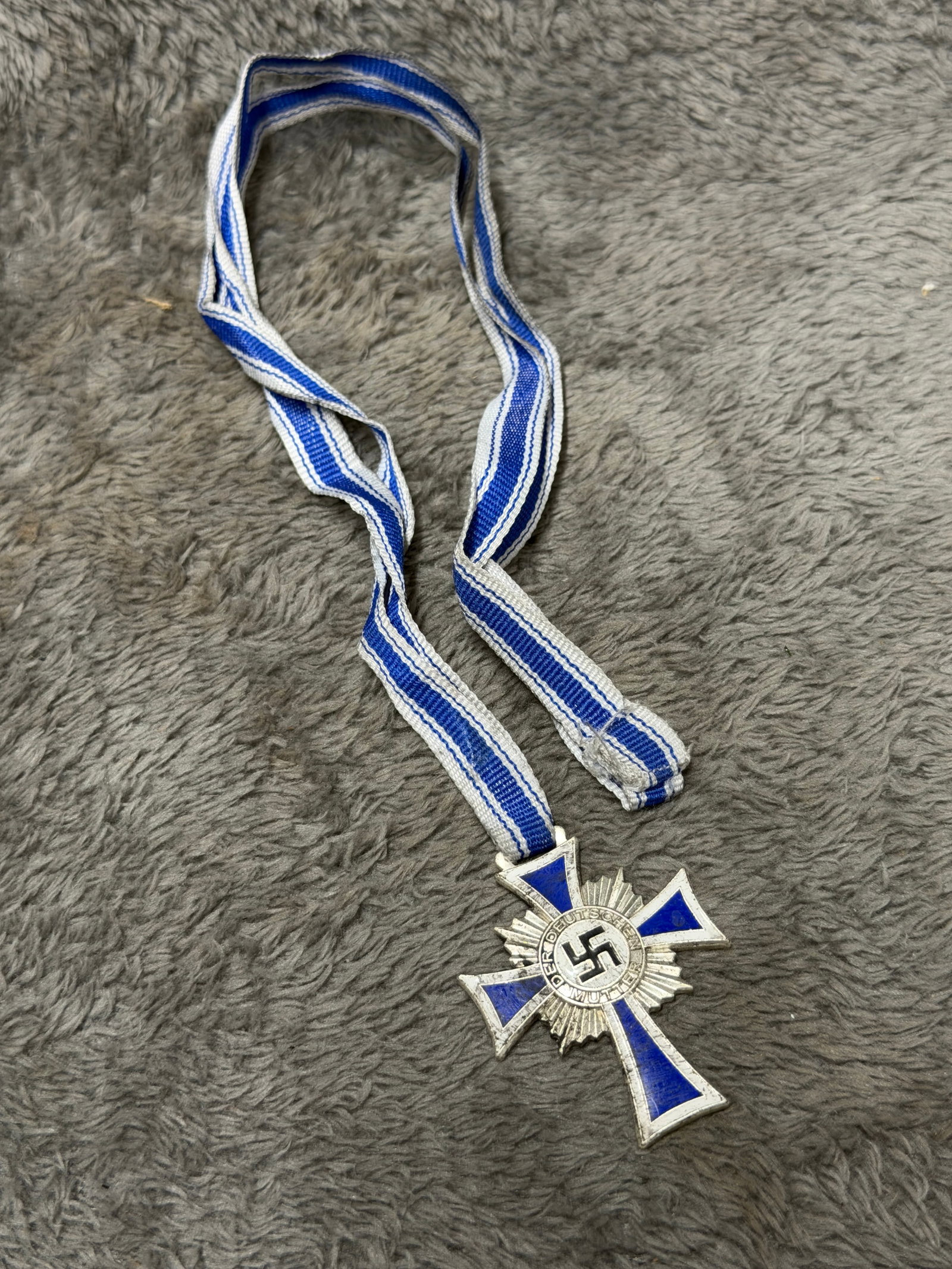 WWII German Mother’s Cross in Silver – Ehrenkreuz der Deutschen Mutter – Blue & White Ribbon: A distinctive WWII German Mother’s Cross in Silver, formally known as the Ehrenkreuz der Deutschen Mutter (Cross of Honor of the German Mother), suspended from its characteristic blue-and-white stri