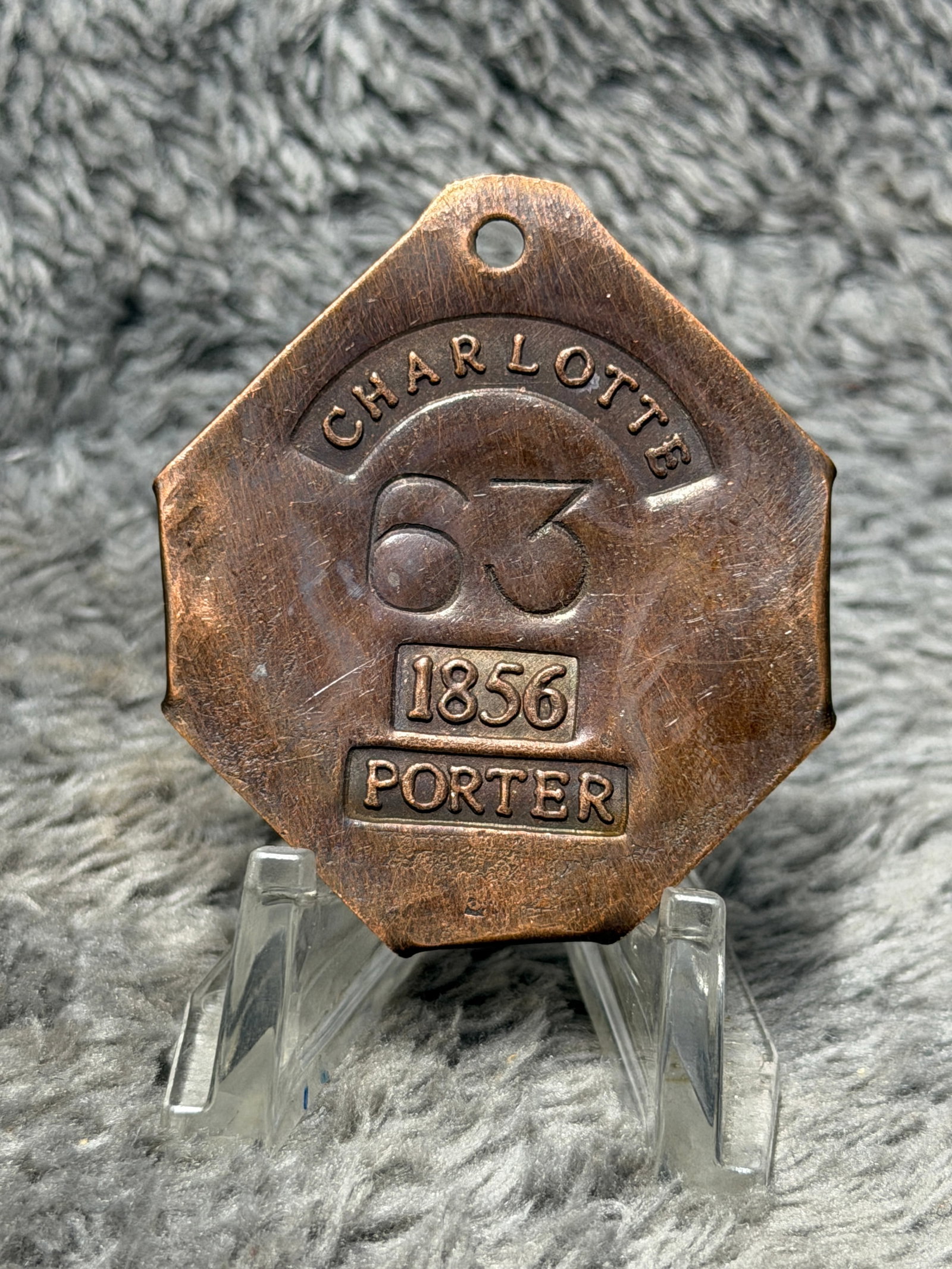 1856 Charleston, South Carolina Slave Hire Tag – Porter No. 63: Mid-19th century Charleston, South Carolina slave hire tag bearing the occupational designation “PORTER” and the date 1856. The multi-sided copper-colored metal tag features a suspension hole 