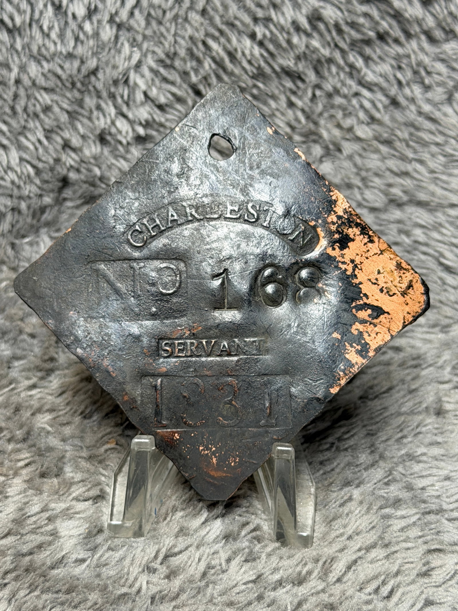 1831 Charleston, South Carolina Slave Hire Tag – Servant No. 168: Charleston, South Carolina slave hire tag dated 1831 and designated “SERVANT,” bearing the identification number 168. The diamond-shaped copper-alloy tag features a pierced suspension hole at 
