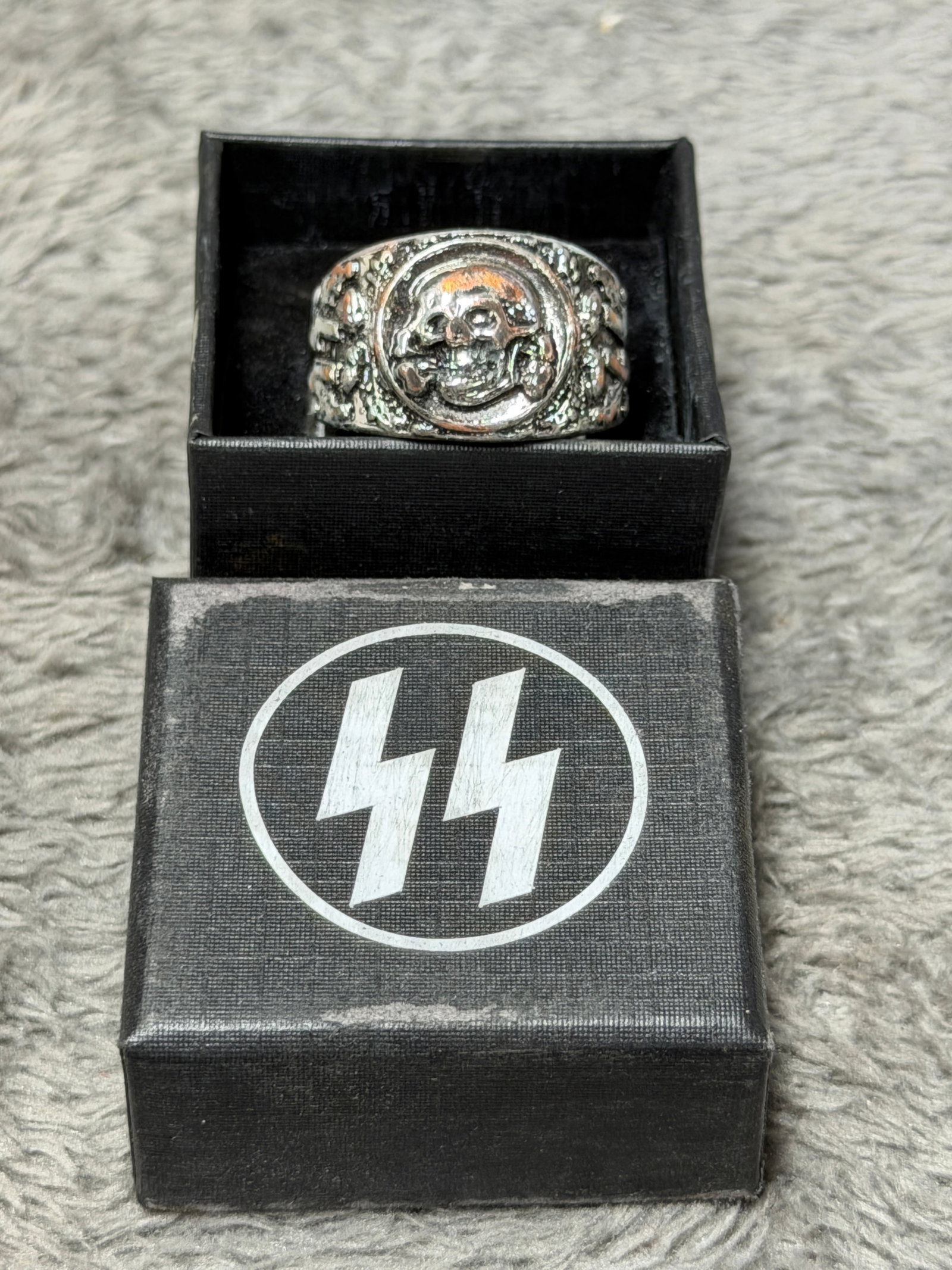 WWII German Waffen-SS Totenkopf Skull Ring with SS Runes & Oak Leaves: WWII German Waffen-SS themed finger ring featuring a prominent raised Totenkopf skull-and-crossbones emblem set within a circular border on the face. The broad shoulders are heavily ornamented with ra