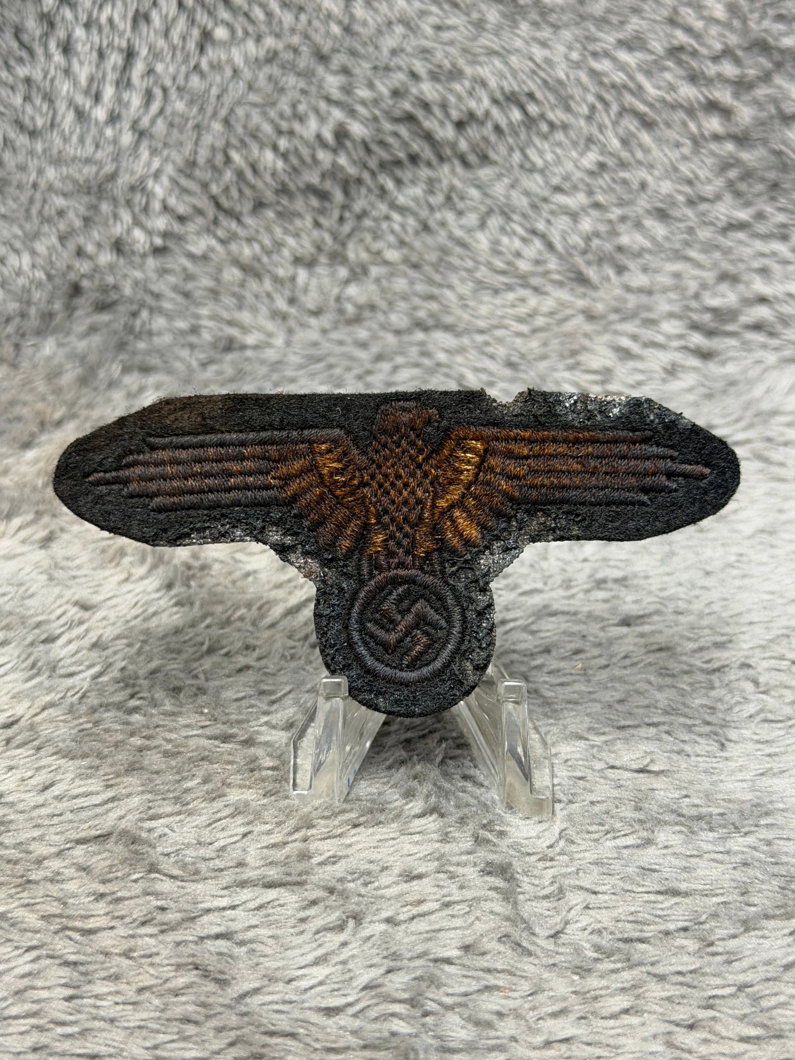 WWII German Waffen-SS Eagle & Swastika Embroidered Uniform Insignia: WWII German Waffen-SS embroidered uniform insignia featuring the distinctive spread-wing SS eagle clutching a circular wreathed swastika beneath its body. The insignia is executed in dark brown to bro