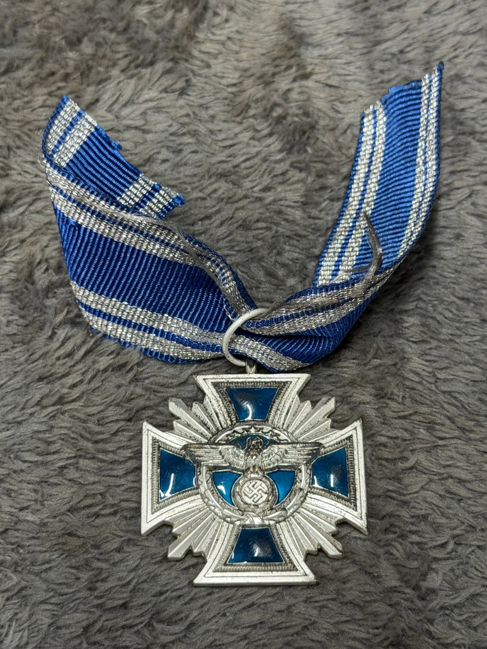 WWII German Treue für Führer und Volk Eagle & Swastika Cross Medal with Ribbon: WWII German decorative cross medal featuring a silver-toned multi-rayed cross with vivid blue enamel panels and a central applied eagle clutching a wreathed swastika. The reverse carries a blue enamel