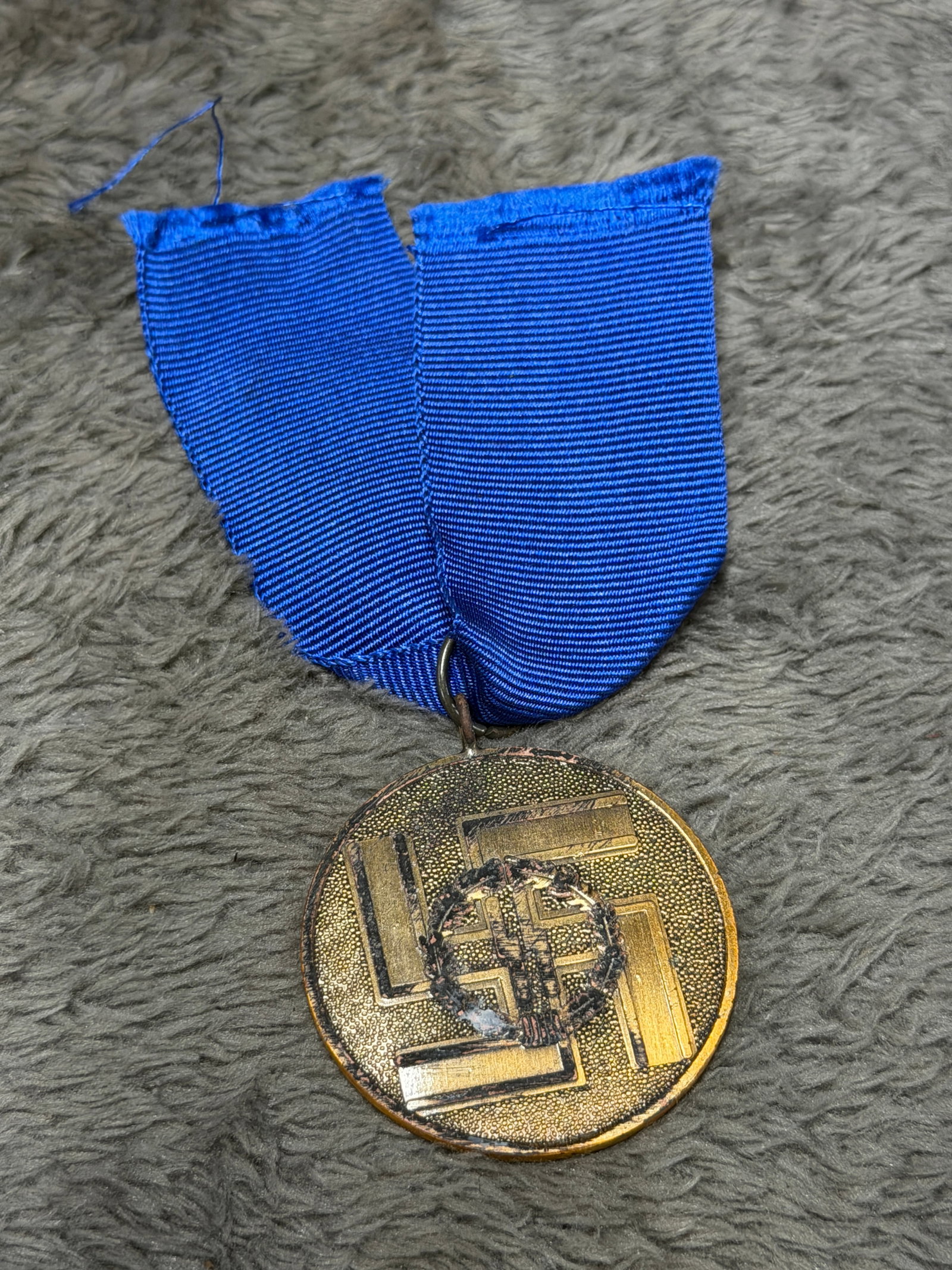 WWII German SS 8-Year Long Service Medal “Für Treue Dienste in der SS?? with Blue Ribbon: WWII German SS long-service decoration consisting of a circular bronze-toned medal suspended from a deep blue ribbed ribbon. The obverse displays a large raised swastika with a central oak-leaf wreath