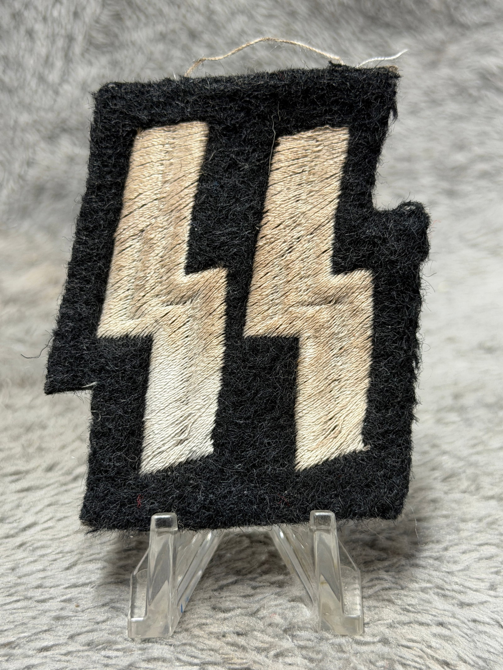 WWII German Waffen-SS Double Rune Sleeve Insignia – Black Wool Embroidered Patch: WWII German Waffen-SS sleeve insignia featuring the distinctive double Sig rune device embroidered in light-colored thread against a black wool field. The large angular runes dominate the rectangular 
