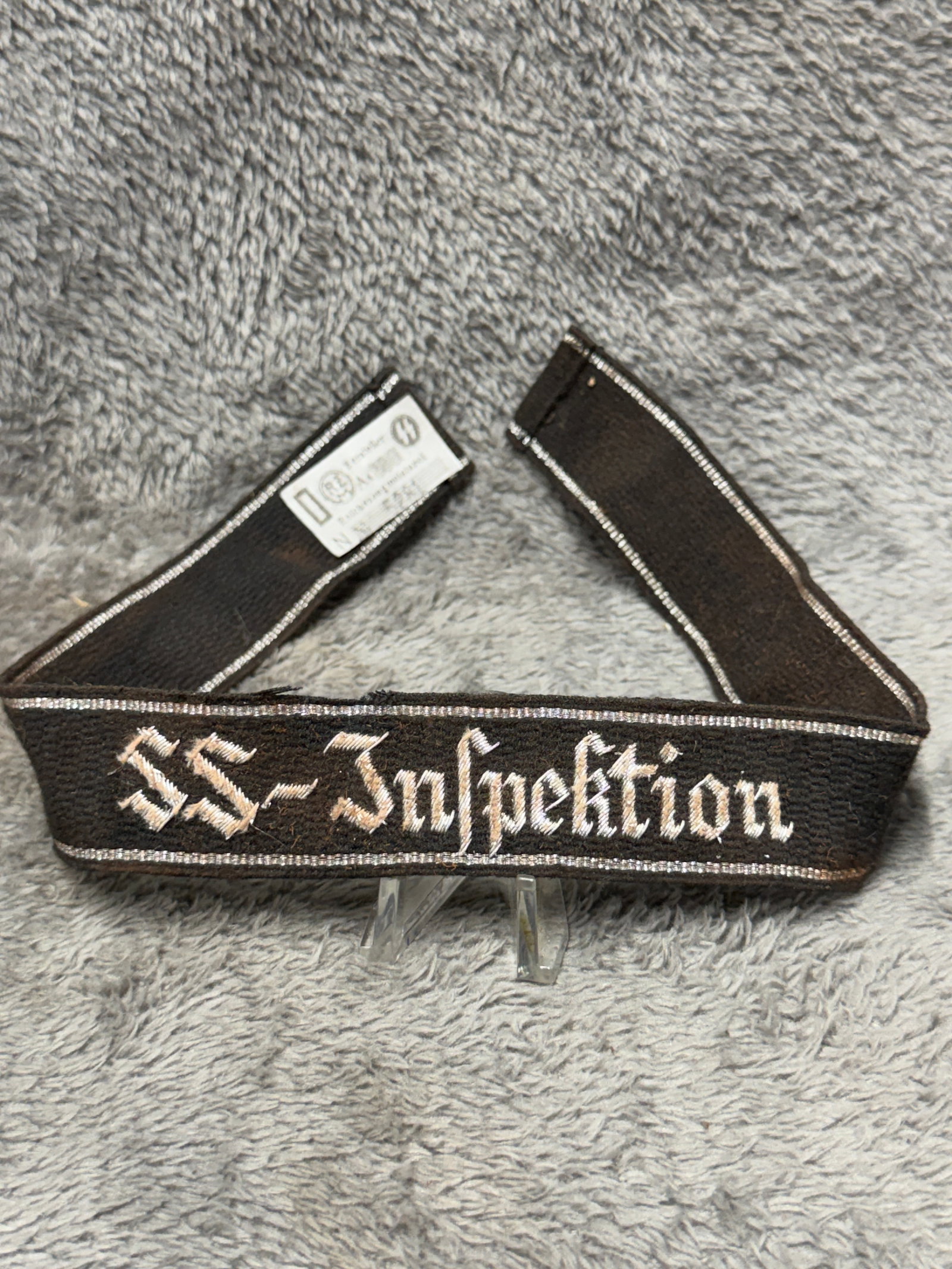 WWII German Waffen-SS “SS-Inspektion?? Cuff Title – RZM Tagged: WWII German Waffen-SS cuff title featuring the designation “SS-Inspektion” embroidered in contrasting light-colored Gothic script across a black woven band. The inscription is bordered along t
