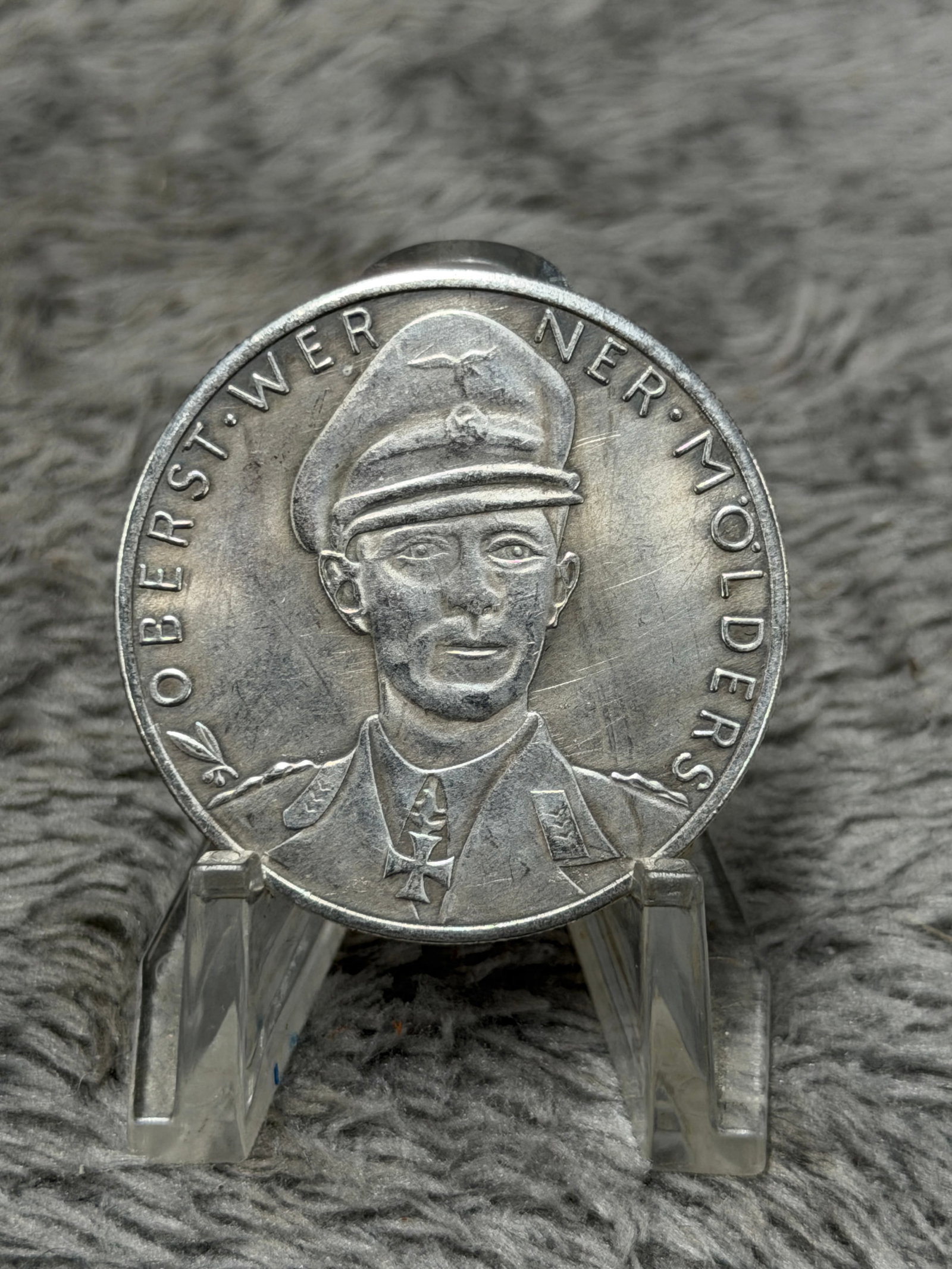 WWII German Oberst Werner Mölders Commemorative Victory Medal – 115 Aerial Victories: WWII German commemorative medal honoring Colonel Werner Mölders, one of Germany’s best-known fighter aces of the period. The obverse features a high-relief uniformed portrait of Mölders wearing hi