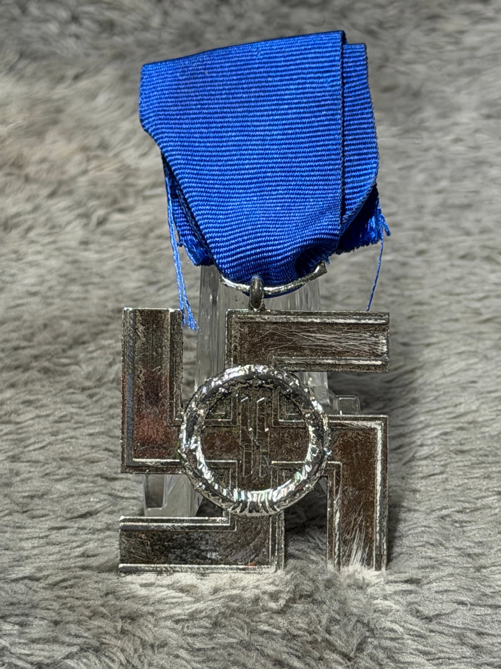 WWII German SS 4-Year Long Service Award Medal with Blue Ribbon: Striking WWII German SS long-service decoration featuring the distinctive silver-finished four-armed swastika-form medal suspended from a deep blue ribbon. The obverse displays the SS runes within a r