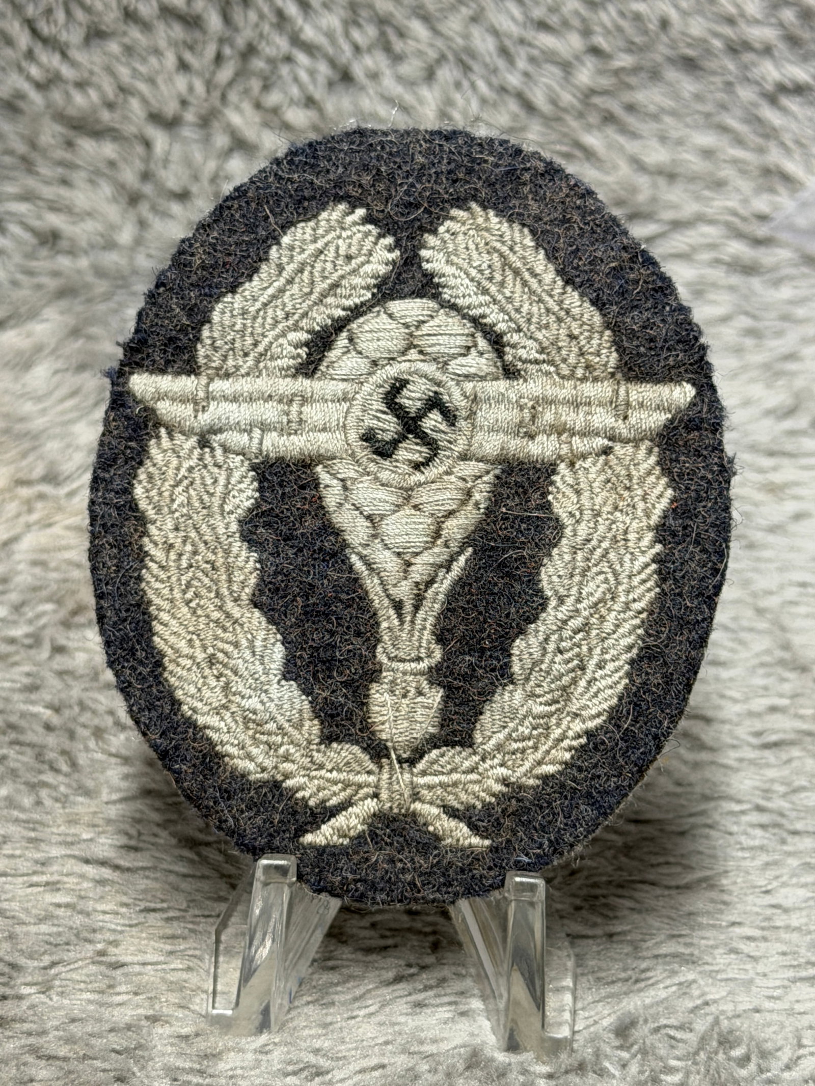 WWII German Luftwaffe Fallschirmjäger Paratrooper Qualification Cloth Badge: Distinctive WWII German Luftwaffe cloth qualification badge featuring the classic Fallschirmjäger paratrooper design embroidered in light-colored thread on a dark oval wool backing. The central compo