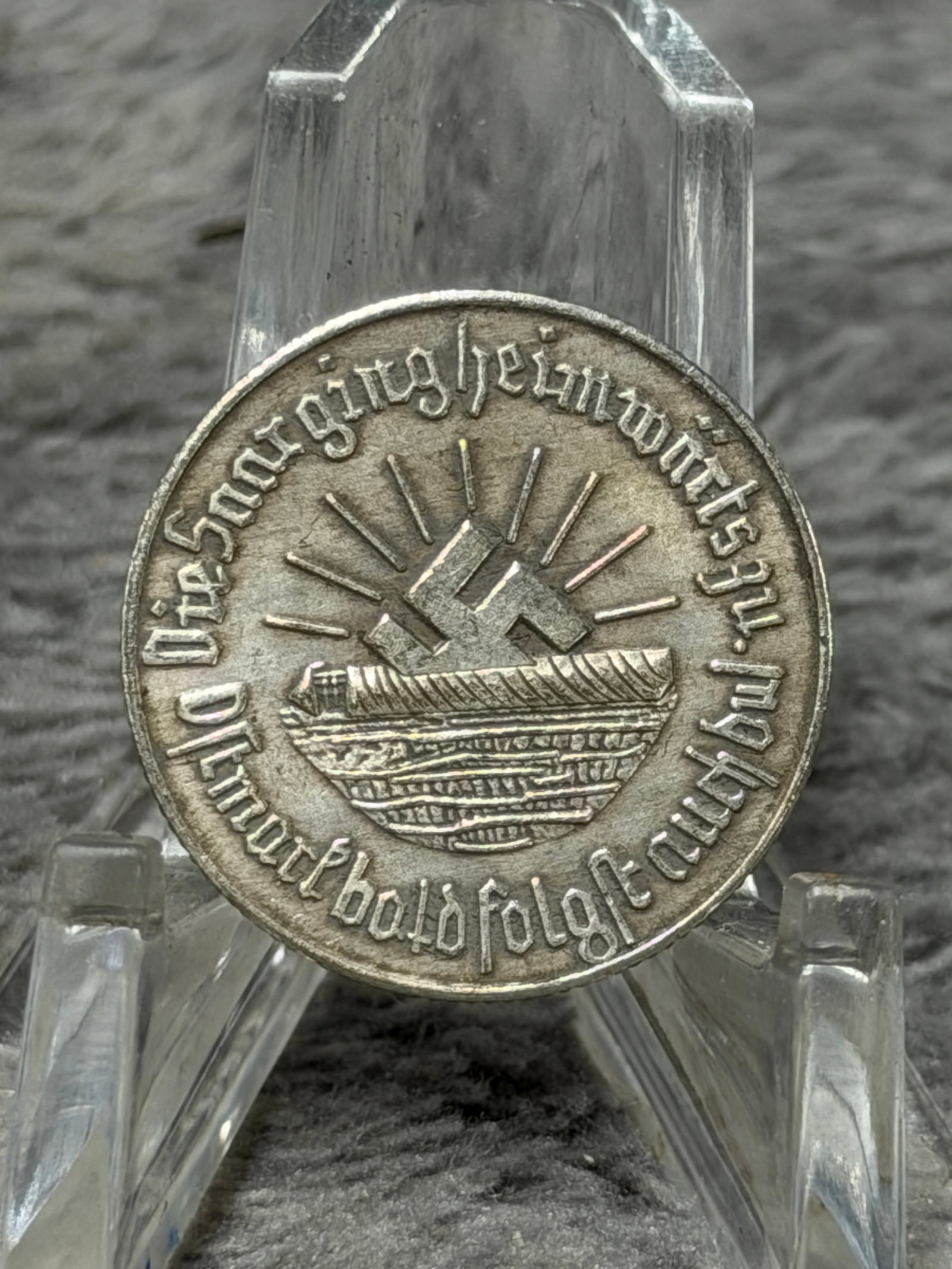 WWII German SA “Ein Schilling?? Winter Relief Donation Token – Nuremberg Rally Motif: WWII-era German SA commemorative donation token featuring a prominent SA emblem on one face with the denomination inscription “EIN SCHILLING” along the lower border. The opposite face displays
