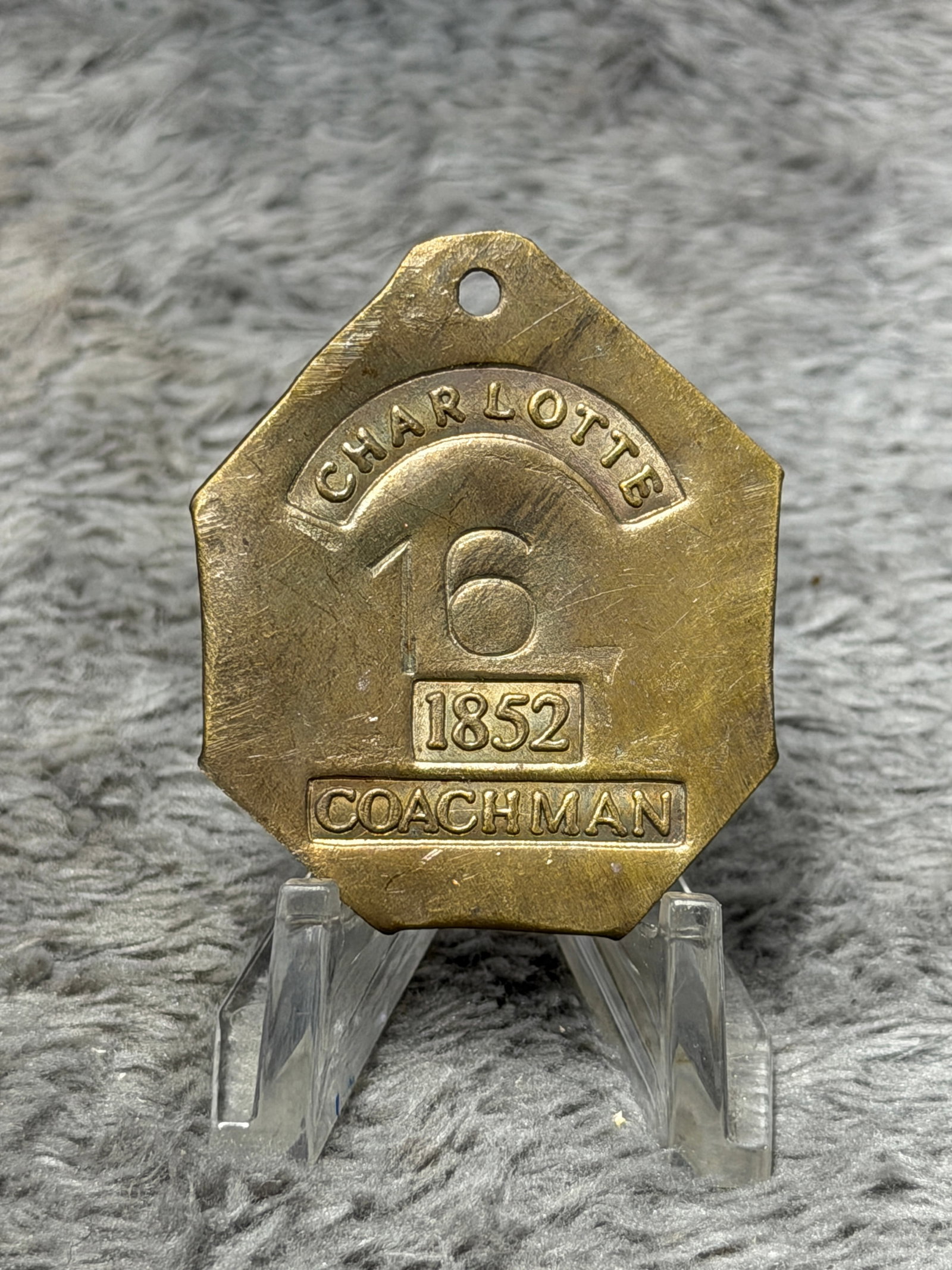 1852 Charlotte No. 16 Coachman Slave Hire Identification Tag – Brass Badge: Mid-19th century brass identification tag attributed to the system of slave-hire and occupational identification, prominently marked “CHARLOTTE” across the upper portion, with the large assign