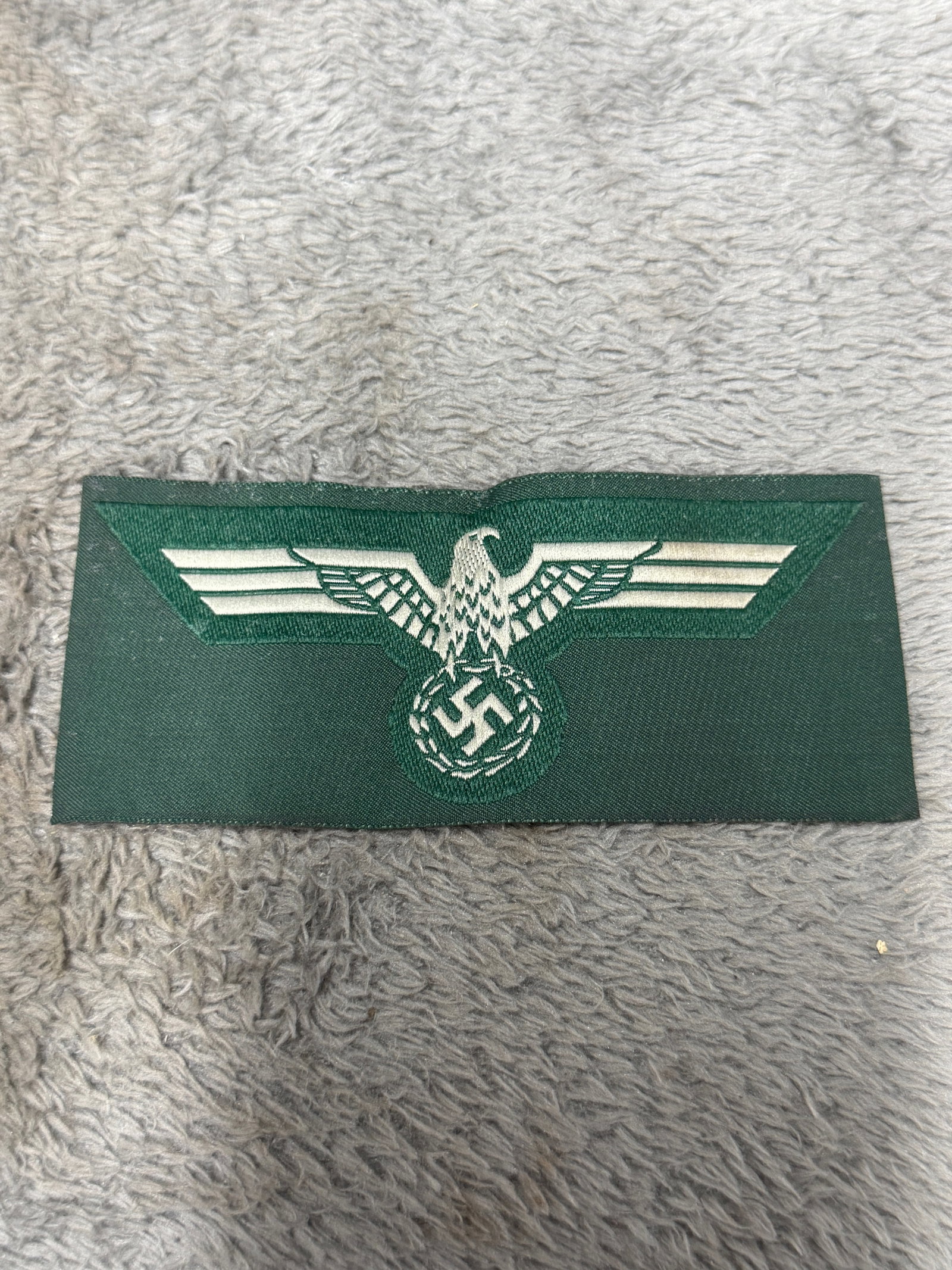 WWII German Heer Army Breast Eagle Insignia on Field-Green Cloth: WWII German Heer Army national breast eagle insignia featuring the characteristic spread-winged German eagle positioned above a wreath enclosing a swastika. The eagle and wreath are executed in contra