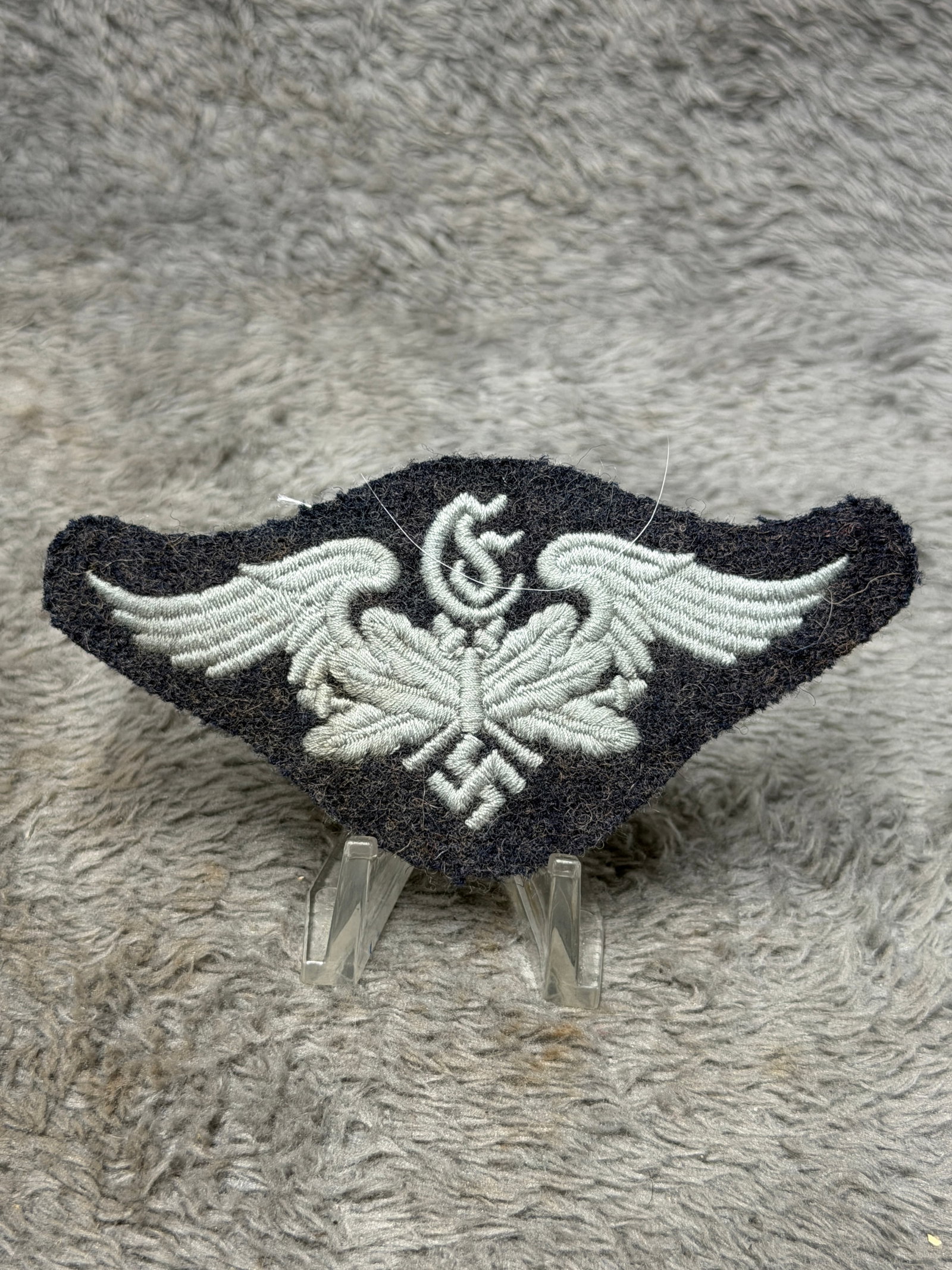 WWII German Luftwaffe Flight Personnel Embroidered Winged Insignia: WWII German Luftwaffe cloth insignia featuring a prominent pair of outstretched embroidered wings above a detailed oak-leaf arrangement and swastika, with an additional stylized device positioned at t