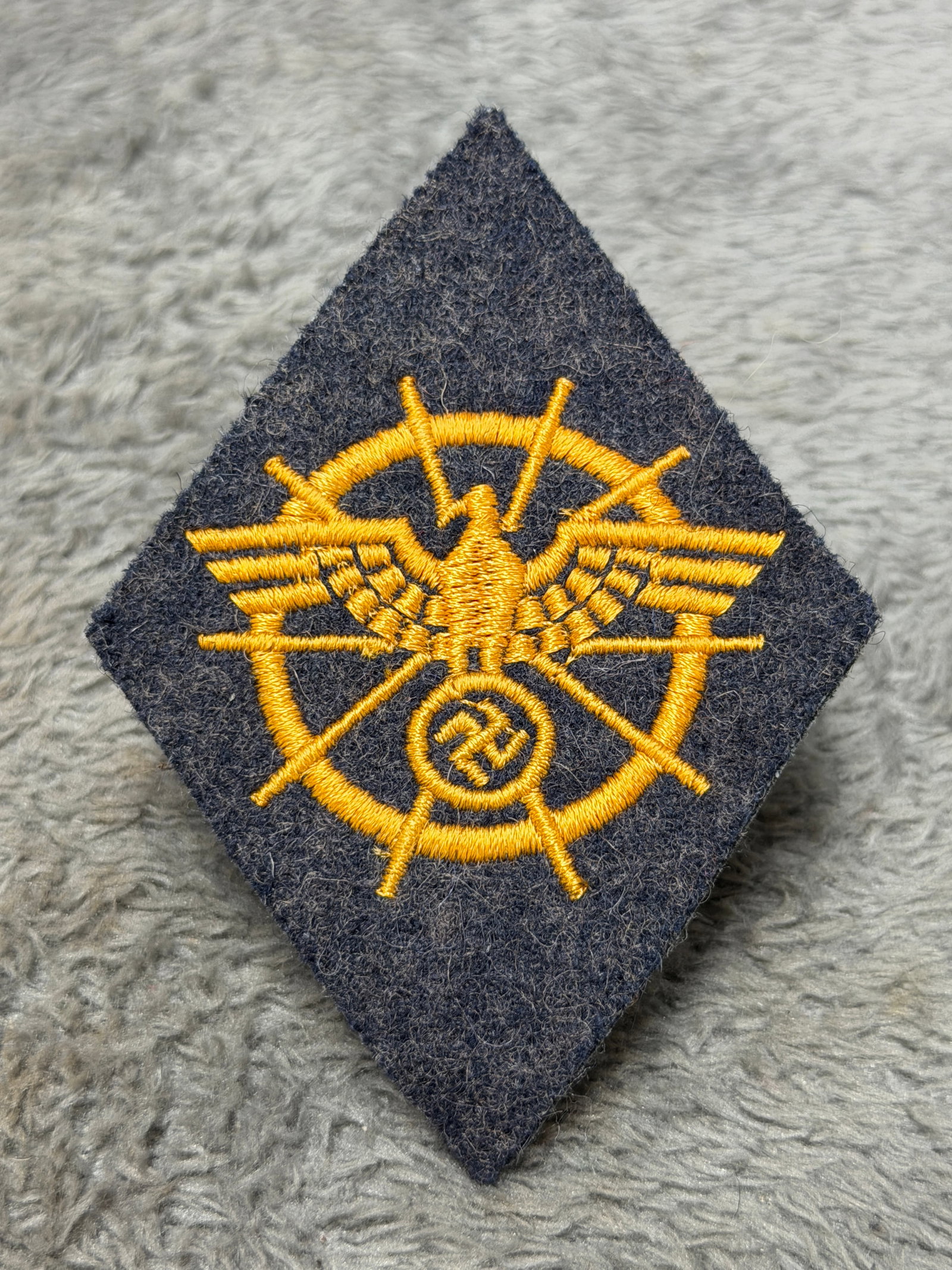 WWII German Kriegsmarine Naval Radio Communications Specialist Sleeve Badge: WWII German Kriegsmarine naval specialty sleeve insignia featuring an elaborate golden-yellow embroidered design on a dark navy-blue diamond-shaped wool backing. The central motif depicts a German eag