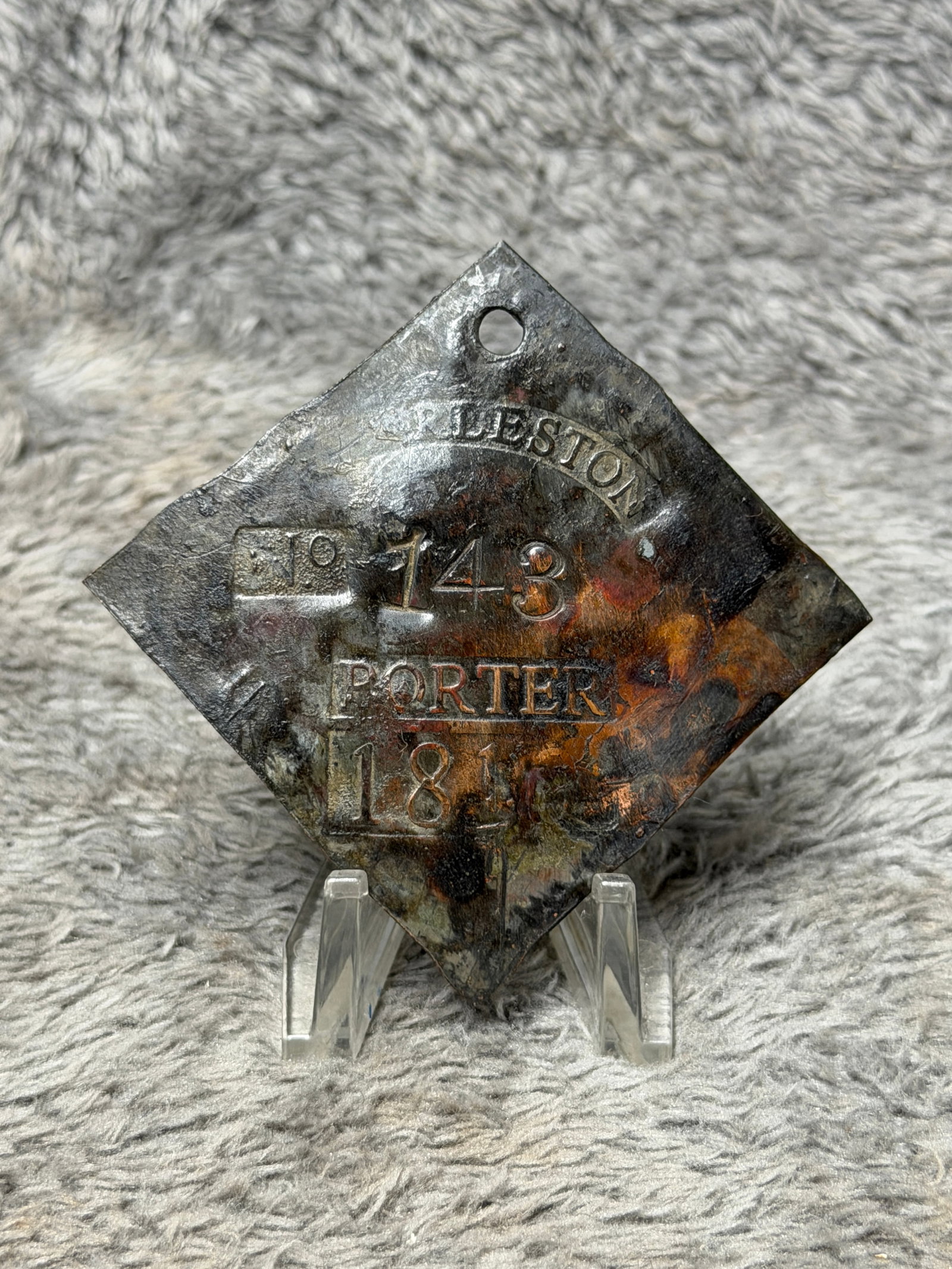 1816 Charleston No. 143 “Porter?? Slave Hire Tag – Early American Identification Badge: Historically significant Charleston slave hire tag dated 1816, fashioned in a diamond-shaped metal form with a suspension hole pierced near the upper point. The face is boldly stamped “CHARLESTON&rd