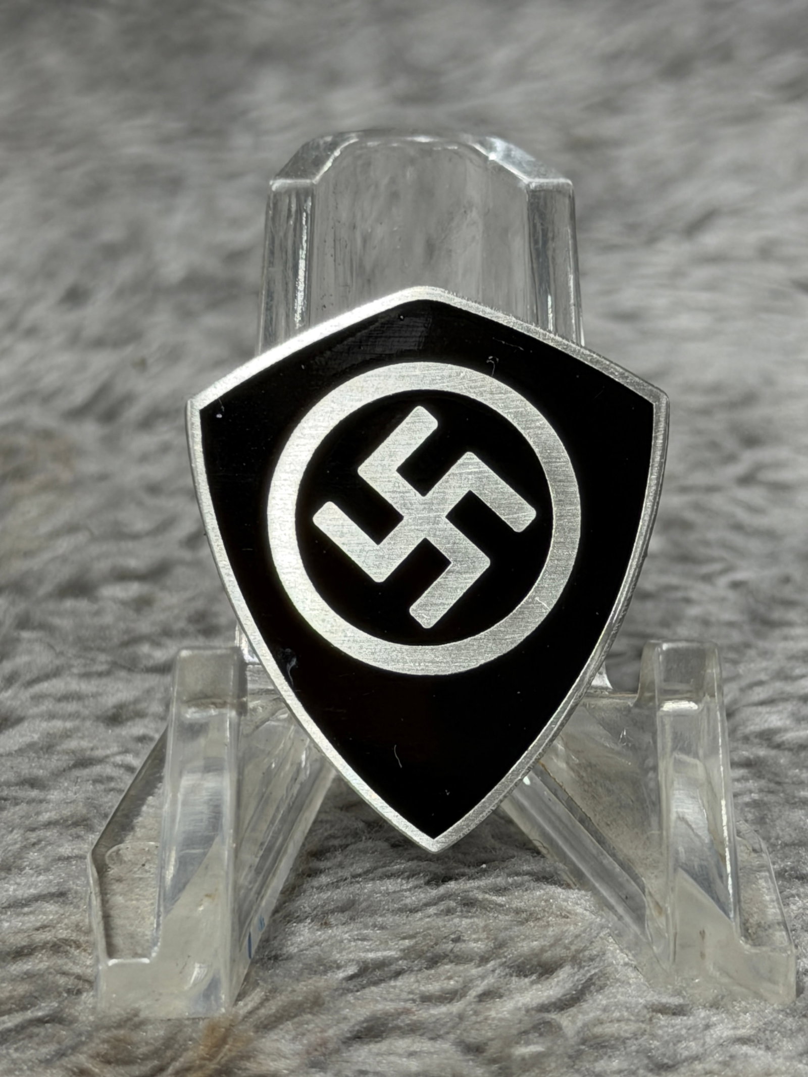 WWII German NSDAP Swastika Shield Membership Pin – Ges. Gesch. Marked: WWII German political membership-style pin featuring a distinctive shield-shaped form with a bold black field and silver-toned border. The center displays a prominent swastika enclosed within a circul