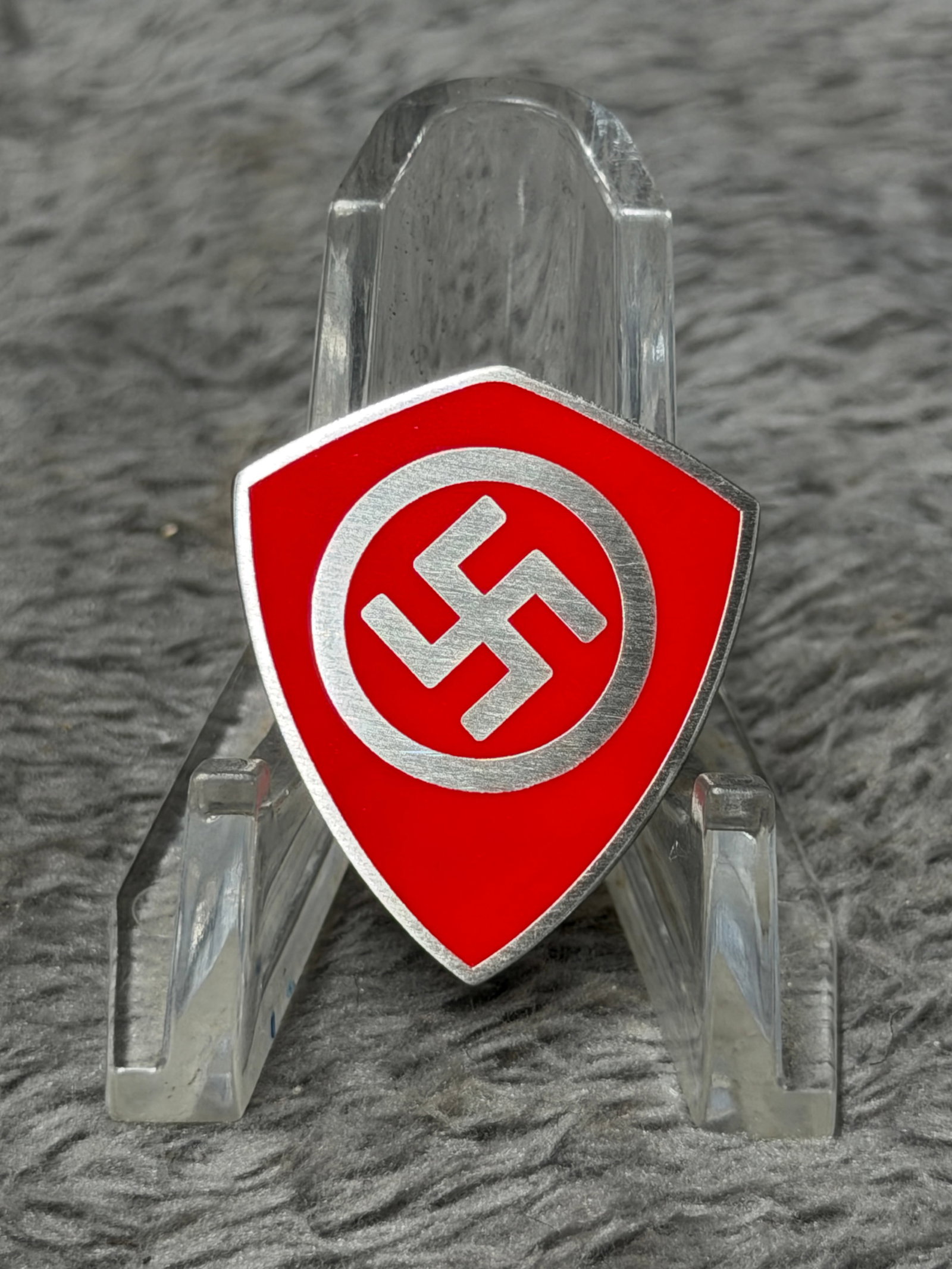 WWII German NSDAP Shield-Shaped Enamel Membership Badge – Ges. Gesch. Marked: WWII German NSDAP-related shield-shaped enamel pin featuring a vivid red field with a silver-tone circular border surrounding the central swastika emblem. The distinctive pointed shield form is finish
