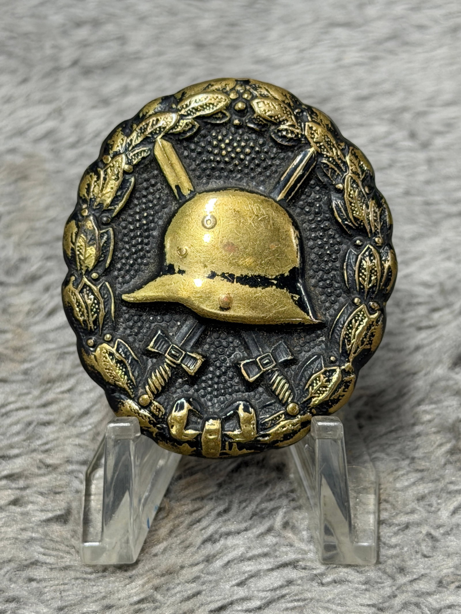 WWI German Imperial Wound Badge in Gold – Stahlhelm & Crossed Swords: WWI German Imperial Wound Badge featuring the distinctive oval design with a German steel helmet positioned prominently at the center over crossed swords, surrounded by a detailed laurel wreath tied a