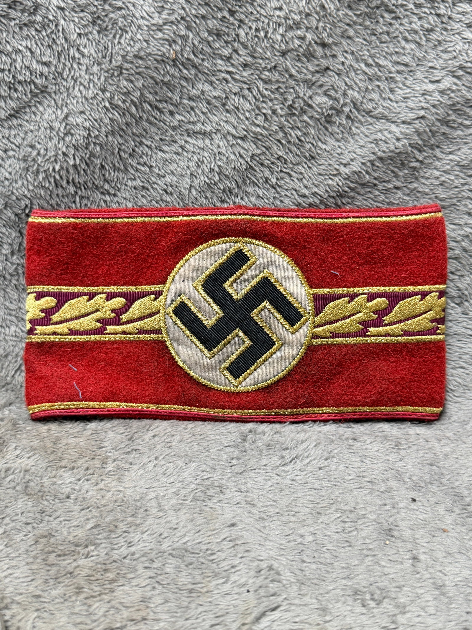 WWII German NSDAP Political Leader’s Gold Oak Leaf Armband With RZM Paper Tag: WWII German NSDAP Political Leader’s armband featuring an elaborate red wool construction with gold-colored piping along the upper and lower borders and a central decorative band of embroidered gold