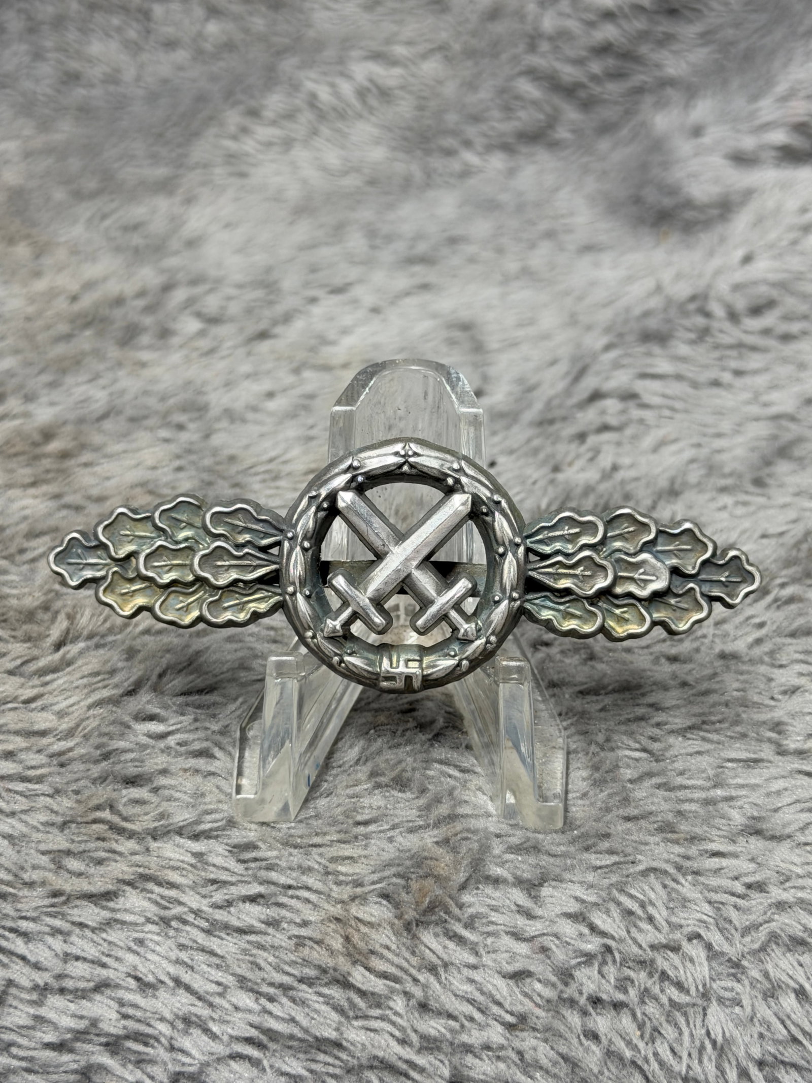 WWII German Close Combat Clasp with Crossed Swords & Oak Leaves: WWII German military combat decoration featuring a prominent central pair of crossed swords enclosed within a circular laurel wreath, flanked on both sides by elongated clusters of deeply detailed oak