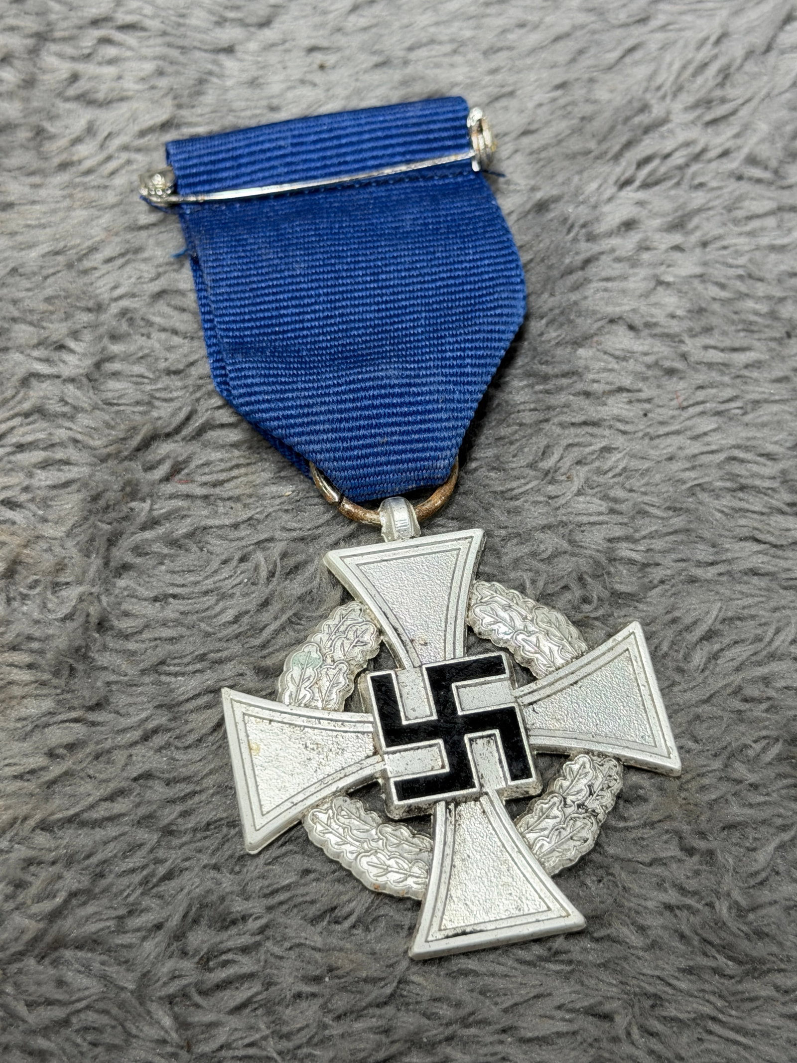 WWII German 25-Year Faithful Service Decoration – Silver Cross with Oak Wreath & Blue Ribbon: Striking WWII German 25-Year Faithful Service Decoration (Treudienst-Ehrenzeichen für 25 Jahre) featuring a silver-toned four-armed cross superimposed over a detailed circular oak-leaf wreath. The ob