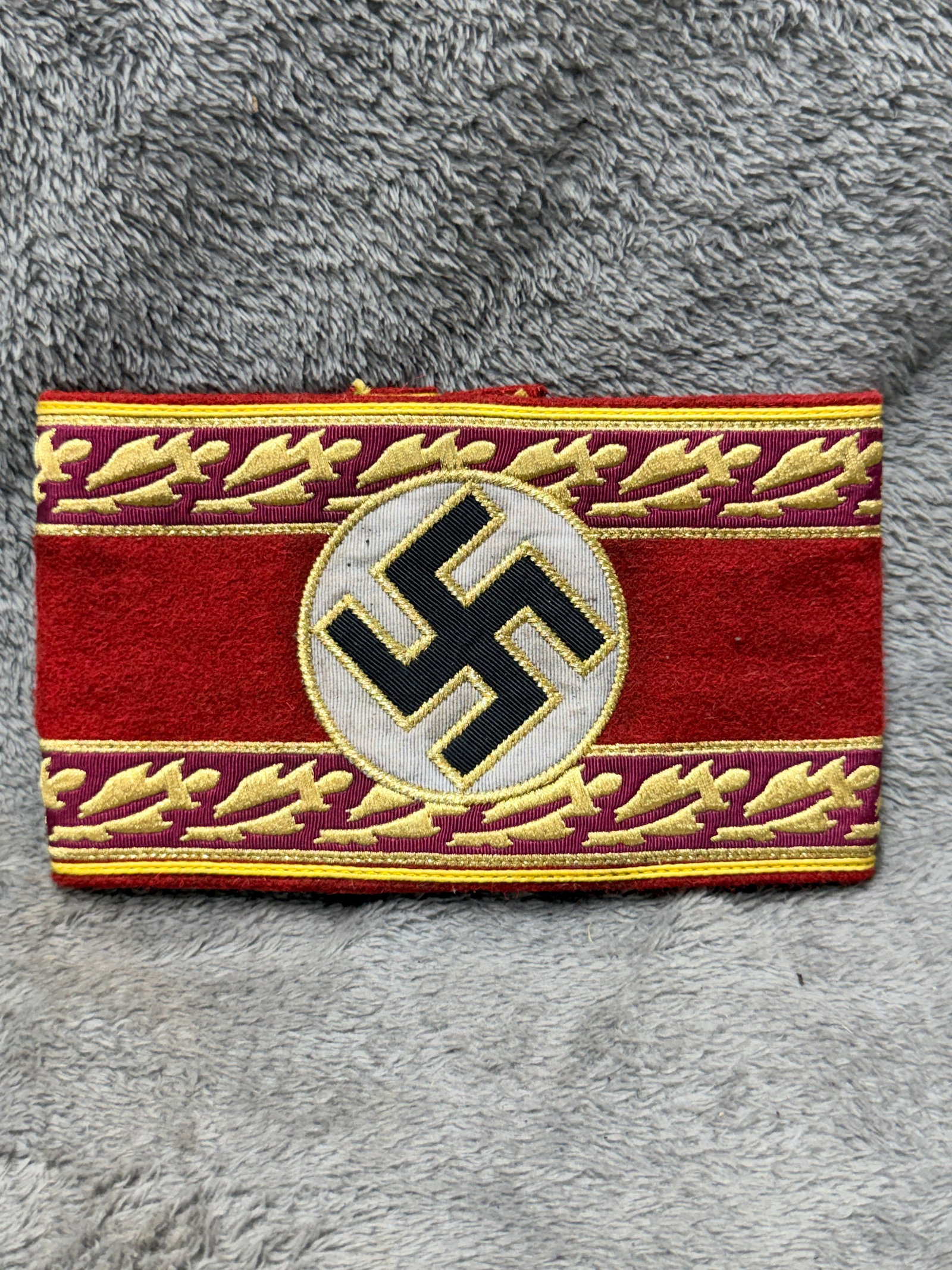 WWII German NSDAP Political Leader Gold Oak Leaf Embroidered Armband: Elaborately constructed WWII German NSDAP political leader armband featuring a broad red wool body with a central white circular field bearing a black swastika, all accented with gold-colored embroide