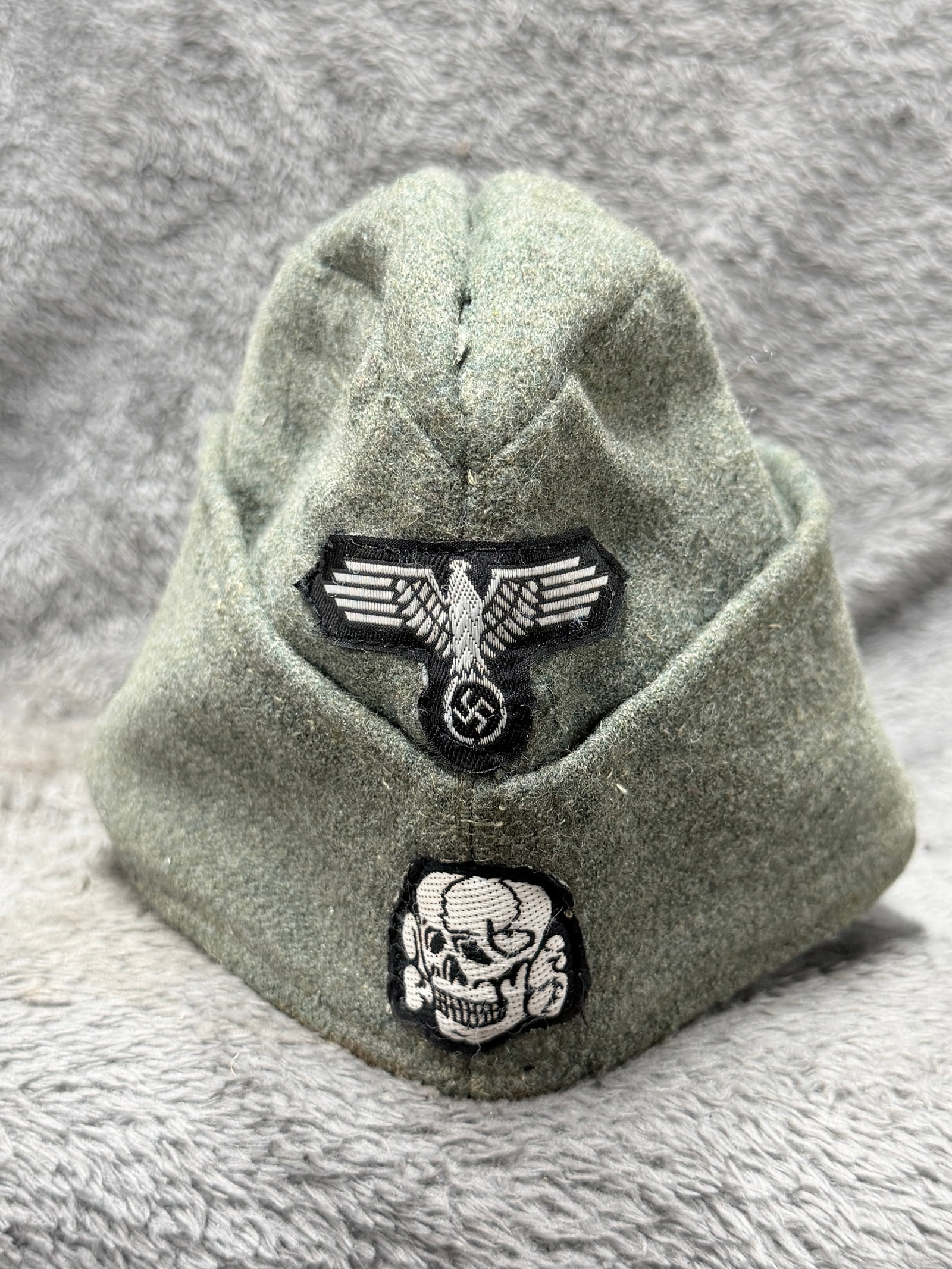 WWII German Waffen-SS Overseas Side Cap with Eagle & Totenkopf Insignia: WWII German Waffen-SS overseas side cap constructed of field-gray wool with the characteristic folding side panels and pointed crown associated with German military field headgear. The front is promin