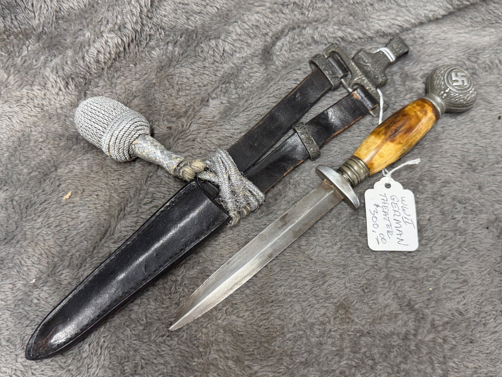 WWII German Hunting Association Dress Dagger with Stag Grip, Swastika Pommel, Leather Hanger &: WWII German dress dagger featuring a polished double-edged blade, warm-toned stag or antler grip, circular metal guard, and an elaborate metal pommel displaying a raised swastika within a wreath of oa