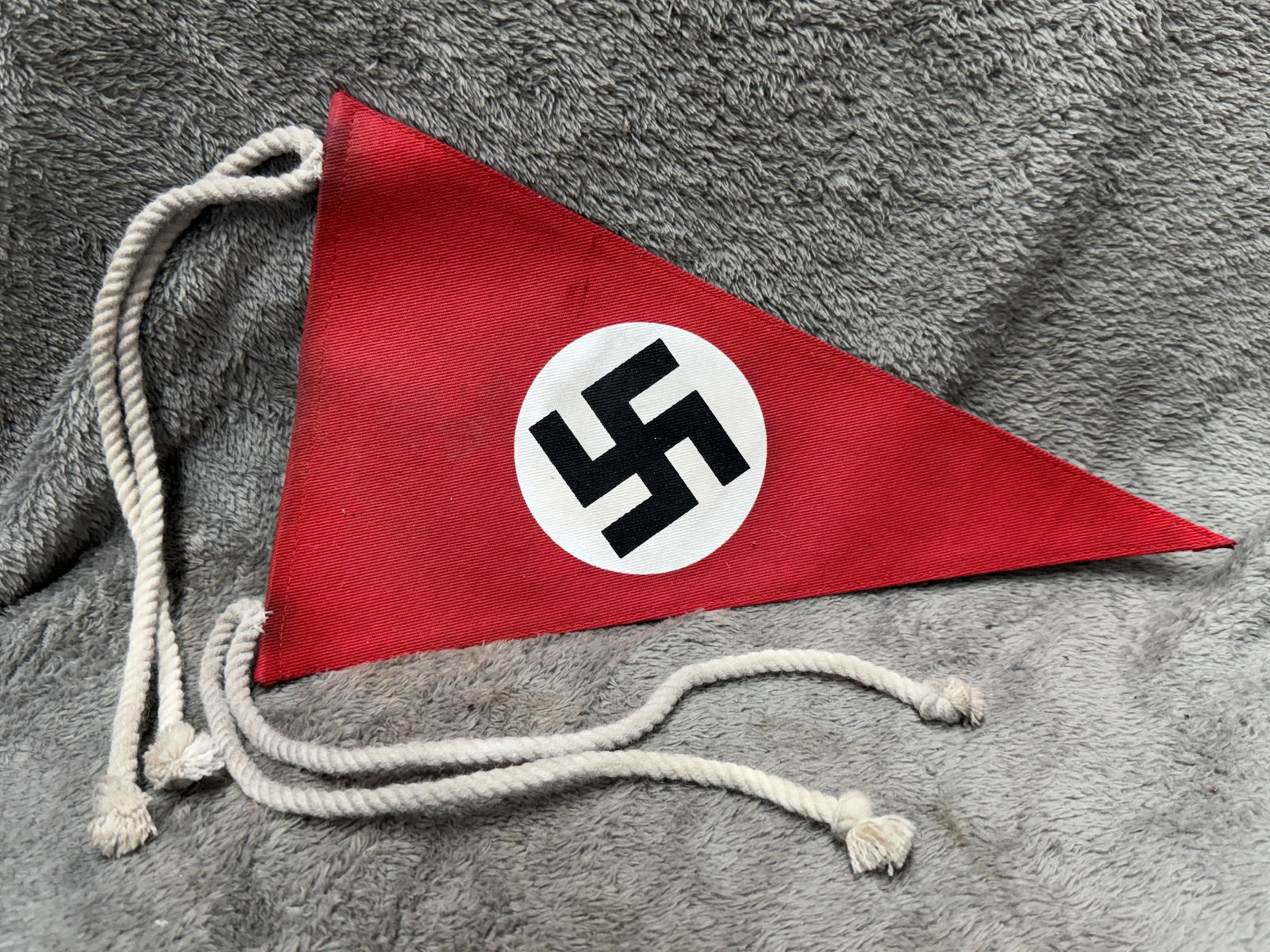 WWII German NSDAP Swastika Vehicle Identification Pennant with Tie Cords: WWII German NSDAP triangular identification pennant constructed of red fabric and prominently displaying a black swastika within a white circular field at the center. The pennant is fitted with long w
