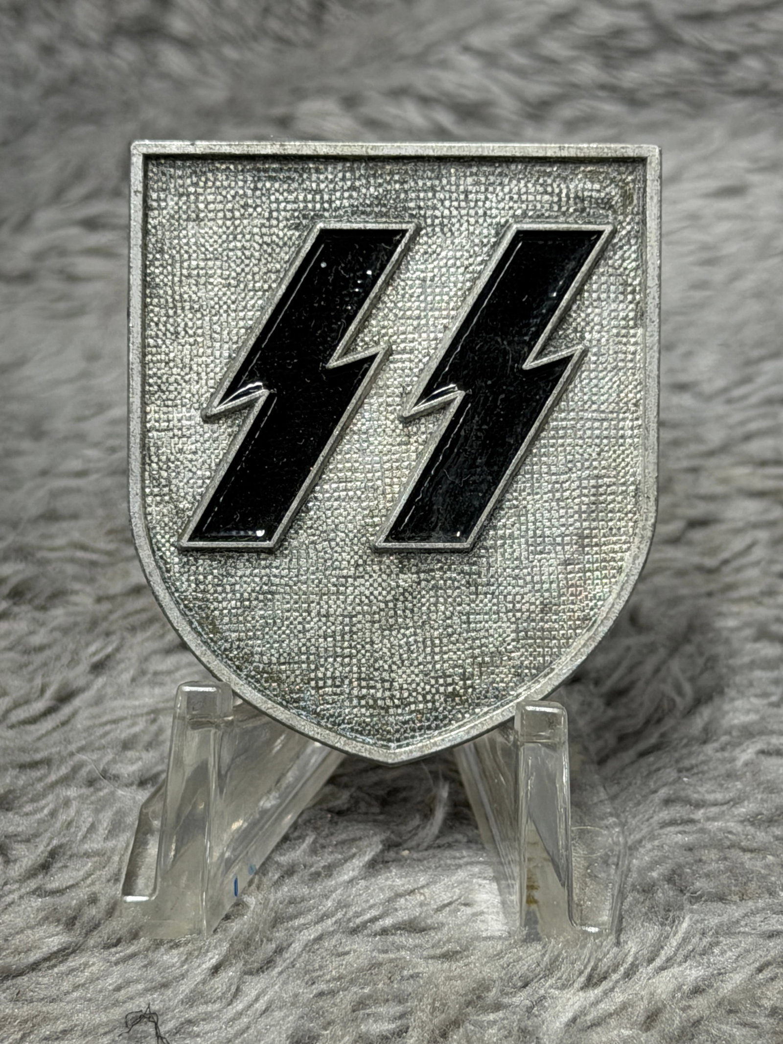 WWII German Waffen-SS Double Sig Runes Metal Shield Insignia – F.P. 1943: WWII German Waffen-SS metal shield insignia featuring the distinctive double Sig rune emblem rendered in glossy black against a textured silver-colored field. The insignia is formed in a large shield 