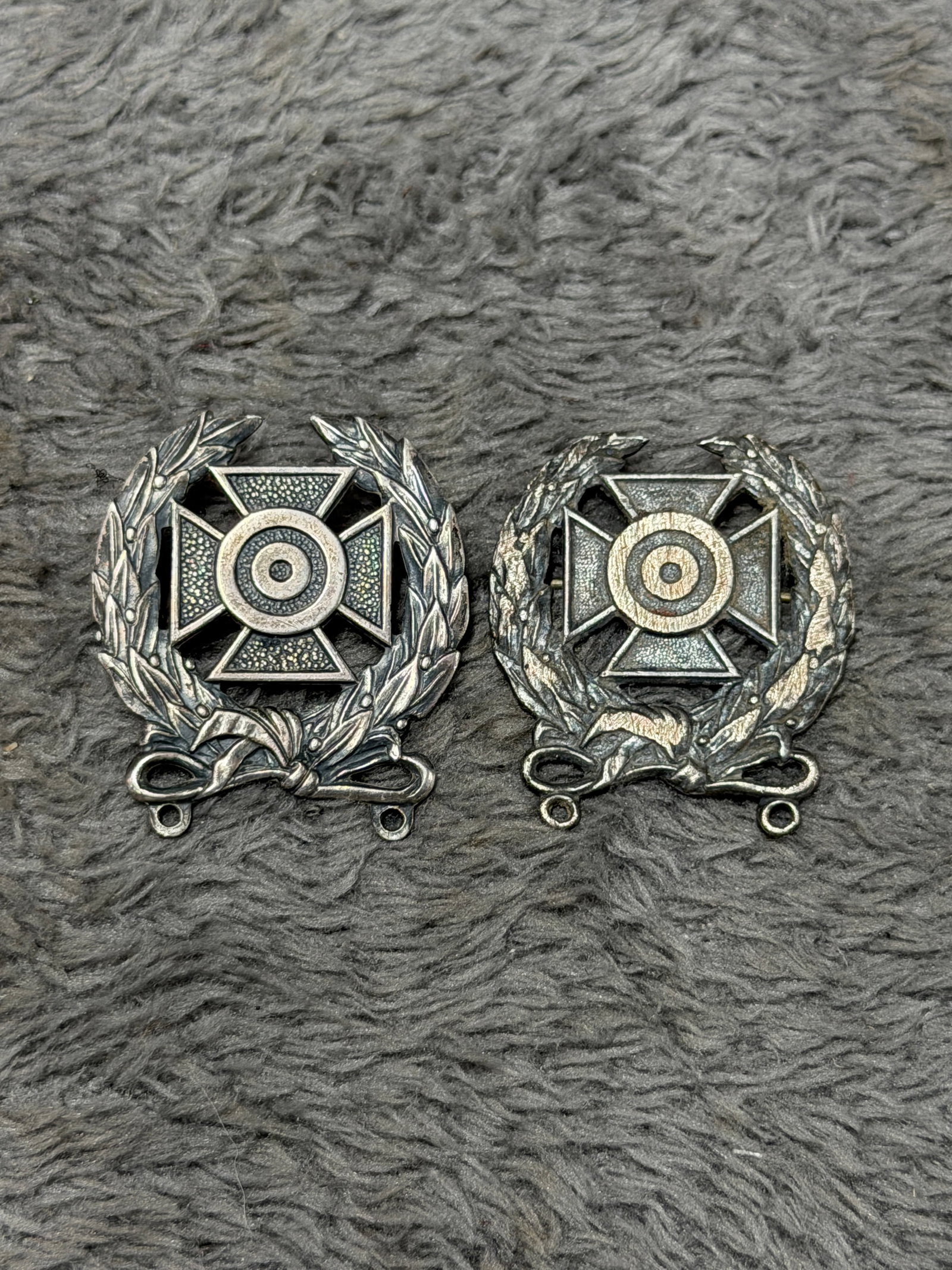 U.S. Military Distinguished Marksman & Pistol Shot Sterling Qualification Badges – Pair: Pair of U.S. military shooting qualification badges featuring the distinctive Maltese-style cross and concentric bullseye target surrounded by detailed laurel wreaths tied at the base. These elaborate