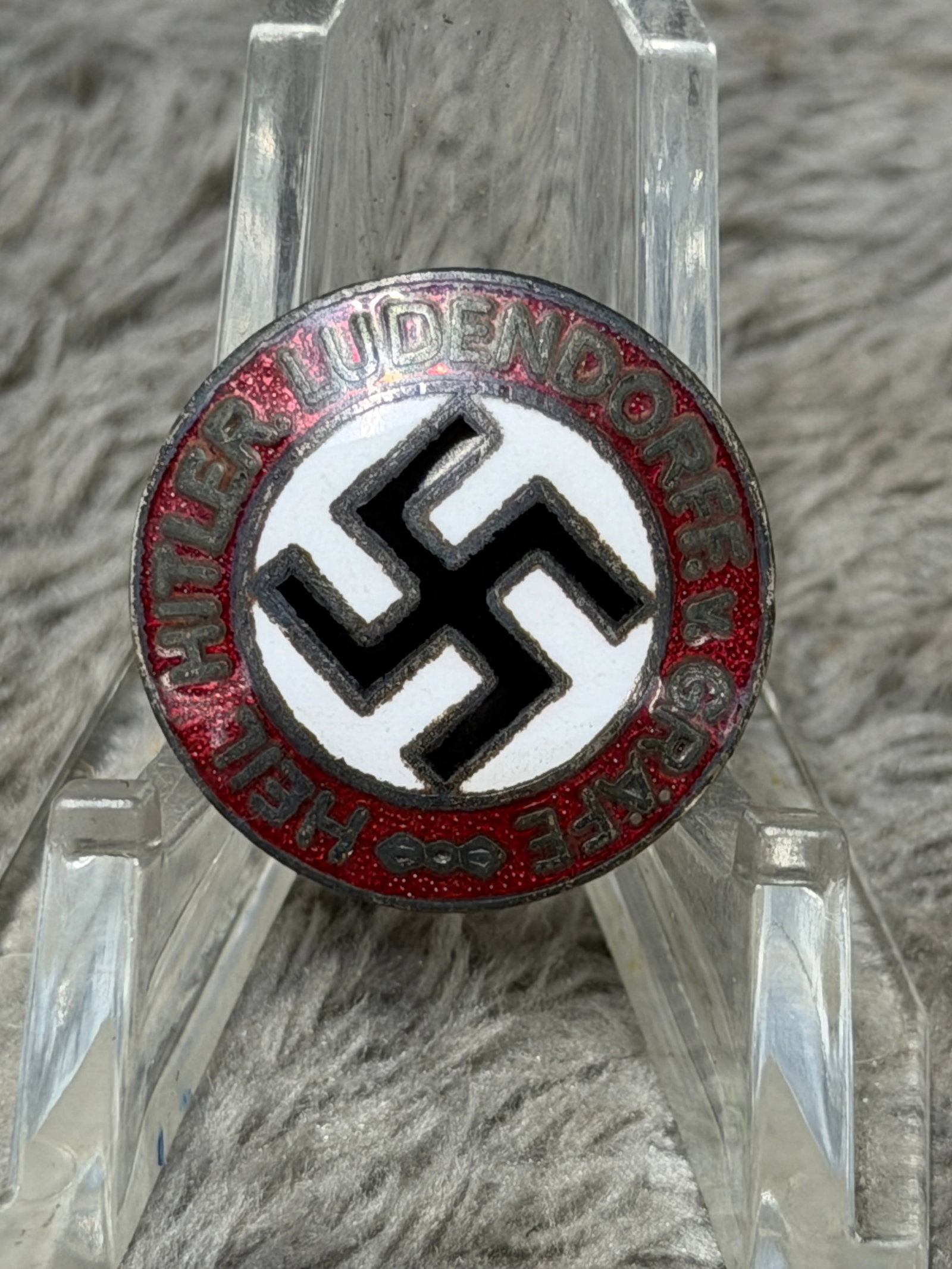 WWII German NSDAP Hitler Youth “Hitler Ludendorff Graefe?? RZM M1/73 Enamel Badge: WWII-era German political commemorative enamel badge featuring a central black swastika against a white circular field, surrounded by a red enameled border bearing the raised inscription “HEIL HITLE