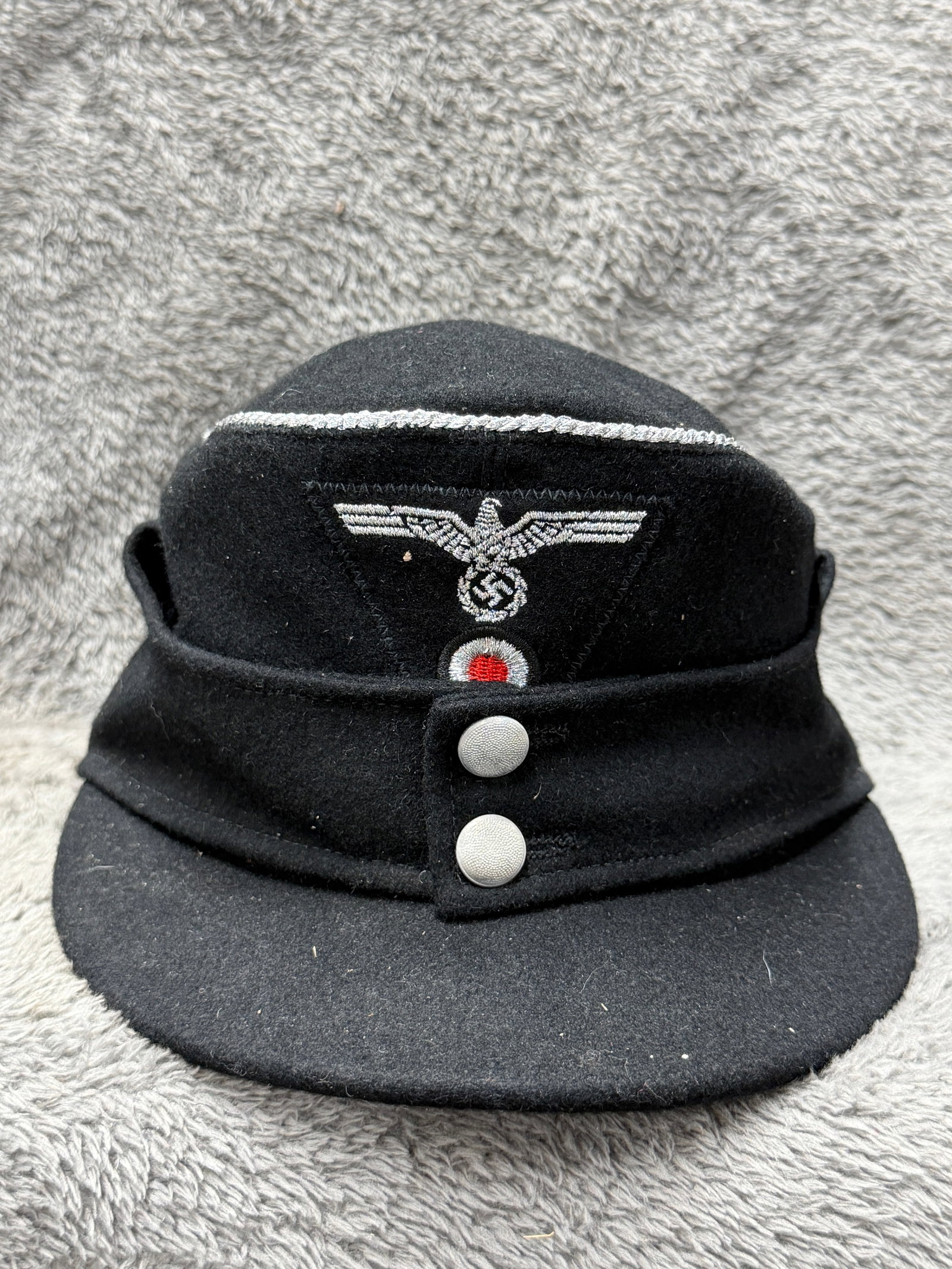 WWII German Heer Panzer Officer Black M43 Field Cap with Silver Piping & Eagle Insignia: WWII German Heer Panzer officer’s black M43 field cap constructed in dark wool and distinguished by silver-colored piping running around the upper crown, a feature associated with officer-grade head