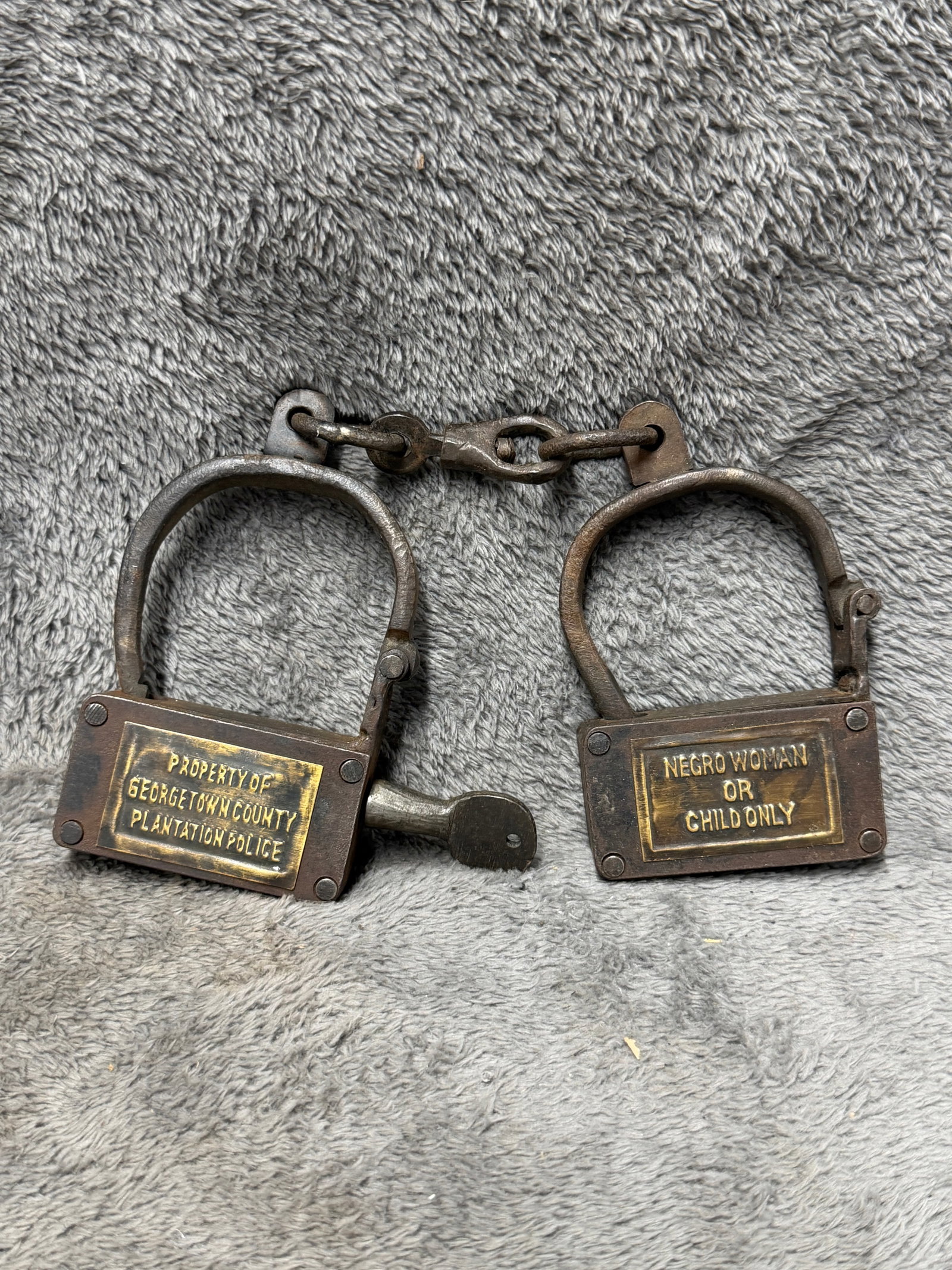 Civil War Era Georgetown County Plantation Police Slave Iron Restraint Shackles with Inscribed Brass: Heavy iron restraint shackles associated with Georgetown County plantation policing, constructed as two substantial hinged wrist restraints joined by an iron chain and central connecting link. Each cu