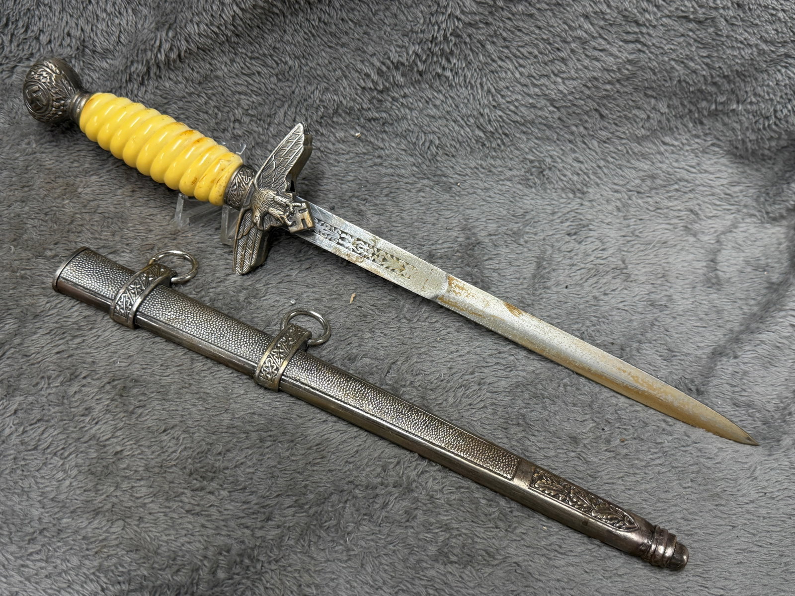 WWII German Luftwaffe Officer Dress Dagger with Eagle Crossguard, Swastika Pommel & Scabbard: WWII German Luftwaffe officer dress dagger featuring an elaborate silver-toned mounted construction with a distinctive ribbed yellow colored grip, oak-leaf decorated fittings and a prominent swastika 
