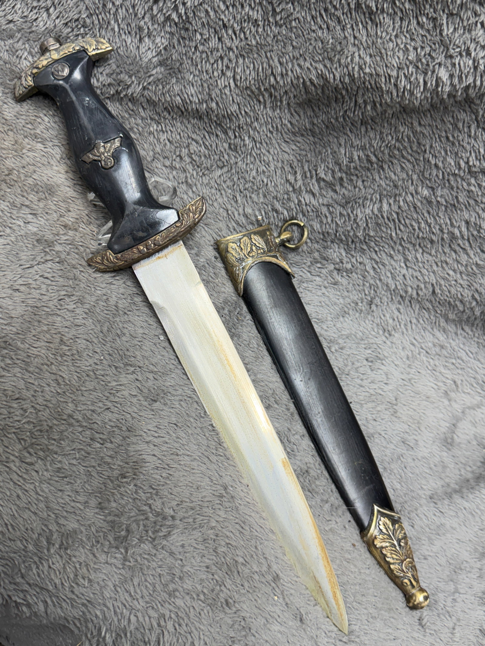 WWII German SS Officer Dress Dagger with Eagle & Swastika Grip Emblem and Black Scabbard: WWII German SS officer dress dagger featuring a substantial black contoured grip fitted with a metal eagle-and-swastika emblem at its center and decorative metal fittings displaying raised oak-leaf an