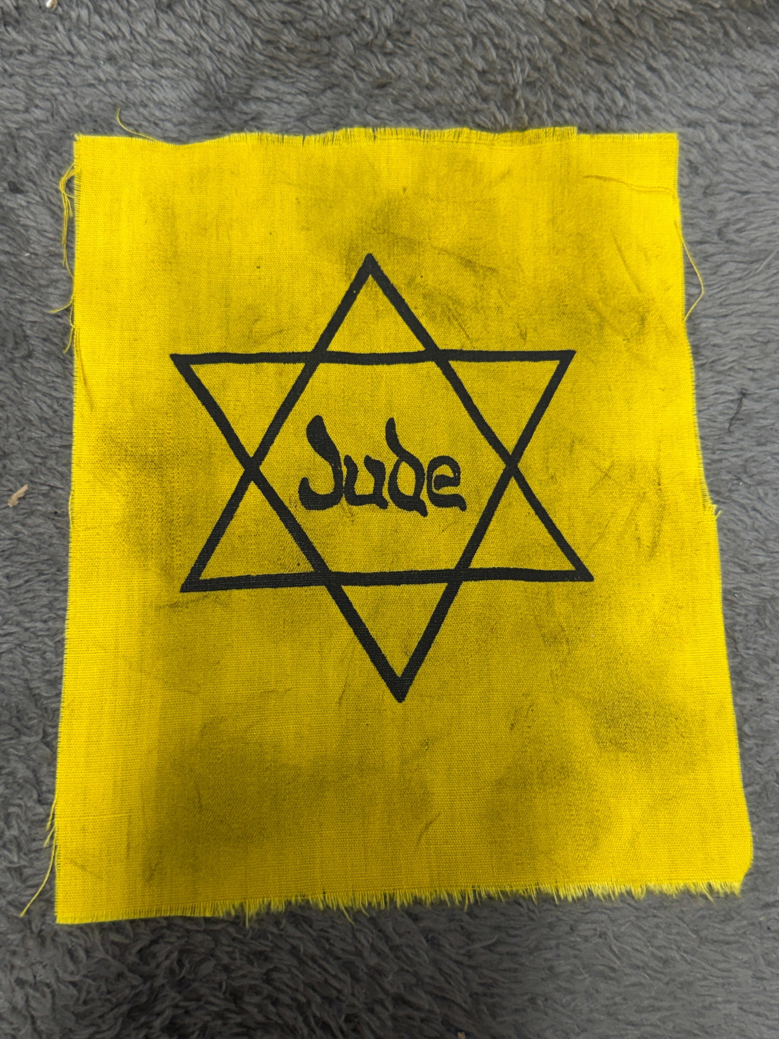 WWII German Jewish “Jude?? Star of David Yellow Cloth Identification Badge: WWII-era German Jewish identification badge constructed from yellow cloth and prominently printed in black with a six-pointed Star of David enclosing the word “Jude,” the German word for “Je