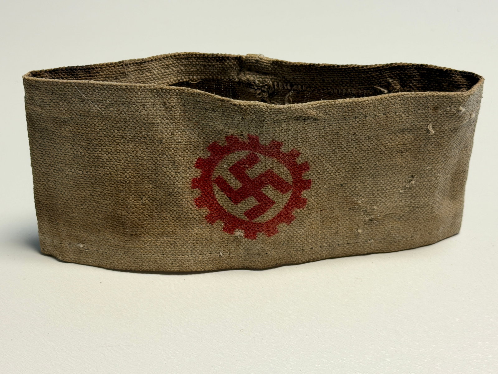 WWII German DAF Deutsche Arbeitsfront Swastika Cogwheel Armband: WWII German Deutsche Arbeitsfront (DAF), or German Labour Front, armband constructed from coarse tan-brown woven fabric and displaying a prominent red cogwheel surrounding a swastika at the center. Th