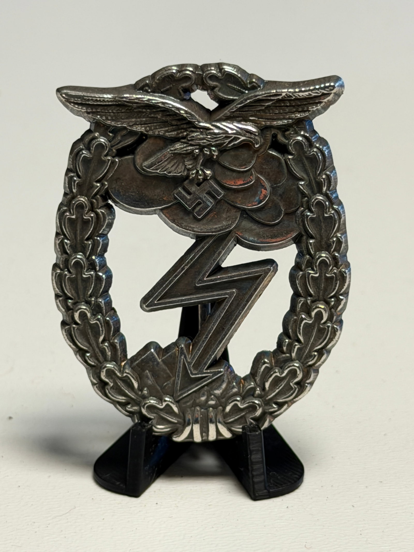WWII German Luftwaffe Ground Assault Badge – GES. GESCH. Marked: WWII German Luftwaffe Ground Assault Badge featuring a dramatic openwork design with a flying Luftwaffe eagle clutching a swastika above storm clouds and a prominent lightning bolt descending toward r