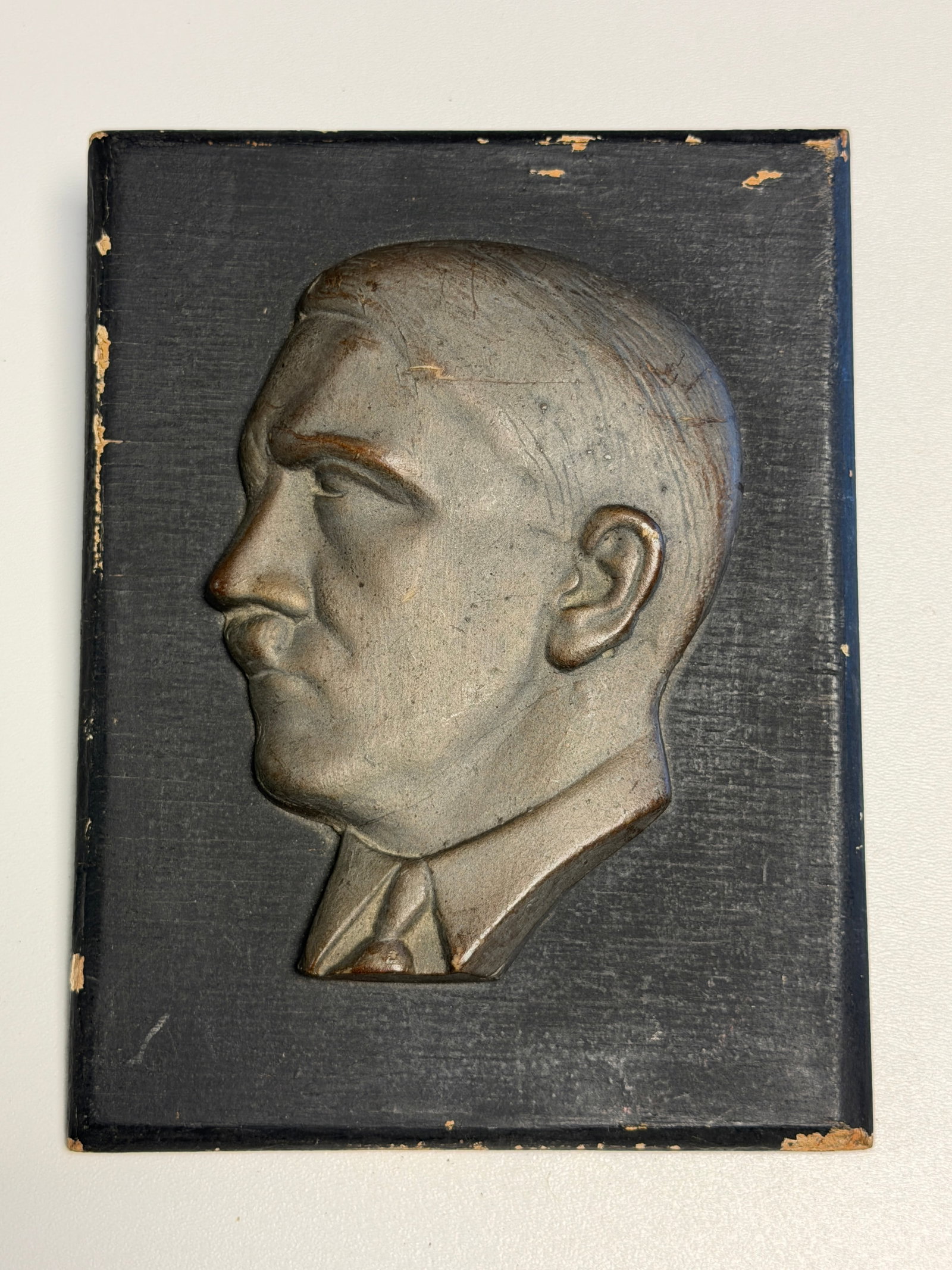 WWII German Adolf Hitler Profile Portrait Relief Wall Plaque: WWII German commemorative display plaque featuring a large raised left-facing profile portrait of Adolf Hitler mounted against a rectangular dark-finished backing board. The sculpted portrait depicts 