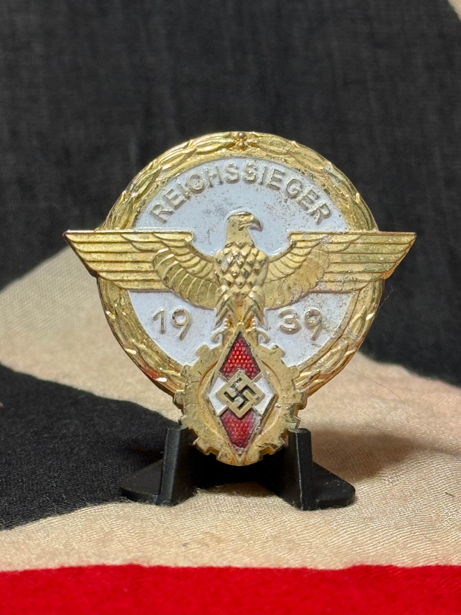 WWII German Hitler Youth 1939 Reichssieger National Competition Badge by G. Brehmer, Markneukirchen: An elaborate WWII German Hitler Youth Reichssieger badge dated 1939, produced in a multi-part appearing design dominated by a large spread-winged eagle positioned across a circular wreath. The upper f