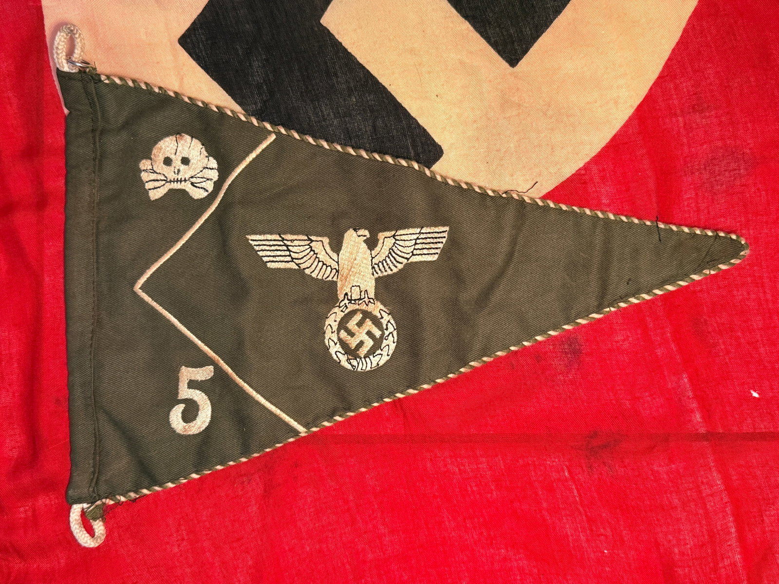 WWII German SS 5th Panzer Division “Wiking" Unit Pennant with Totenkopf & Eagle: A triangular German SS unit pennant executed in dark fabric with contrasting embroidered designs and decorative twisted edging. The central field prominently displays a spread-wing German eagle positi