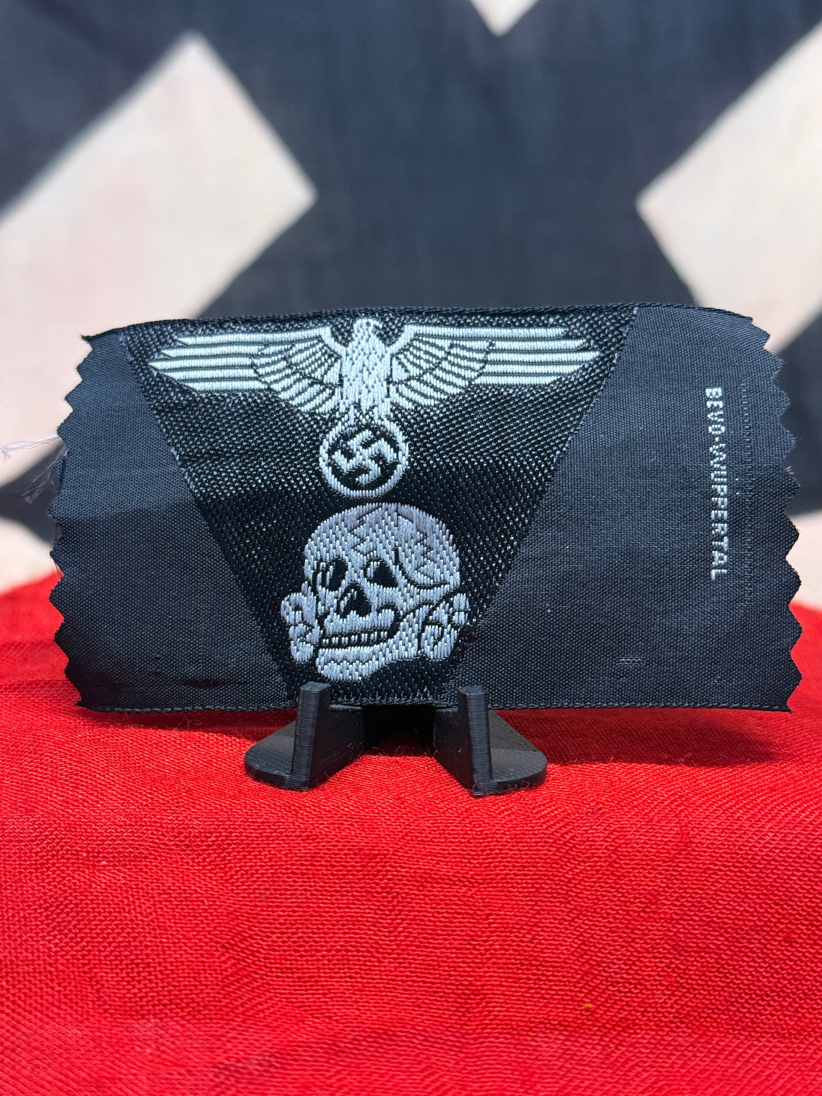 WWII German SS Totenkopf & Eagle Embroidered Cloth Insignia – BeVo-Wuppertal Marked: WWII German SS cloth insignia incorporating two of the organization’s most recognizable devices: a spread-wing eagle clutching a wreathed swastika above an embroidered Totenkopf skull-and-crossbones