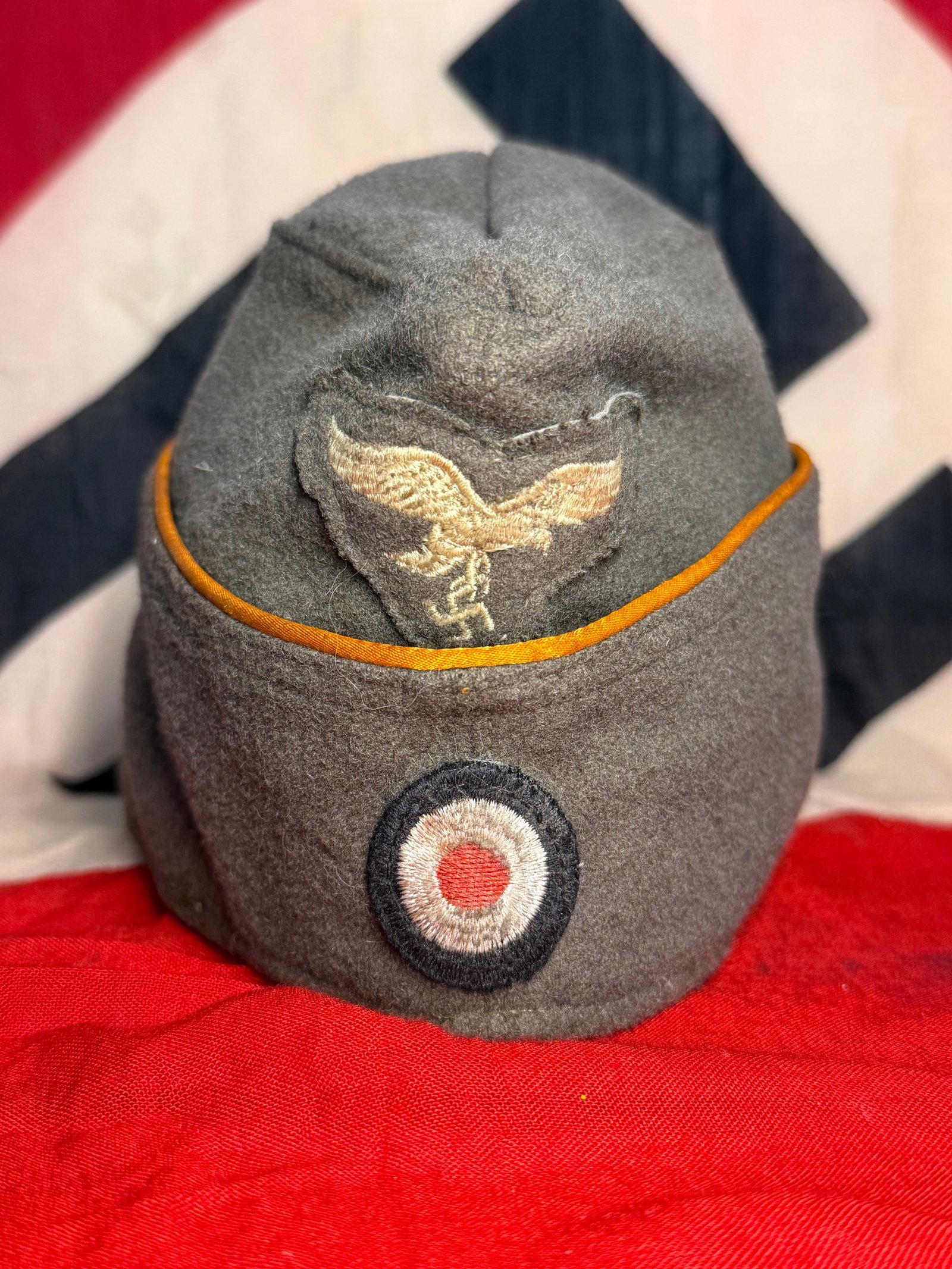 WWII German Luftwaffe Overseas Field Cap with Yellow Waffenfarbe Piping & Eagle Insignia: A WWII German Luftwaffe overseas field cap constructed from field-gray wool and distinguished by contrasting golden-yellow piping around the upper edge. The front carries an embroidered Luftwaffe eagl