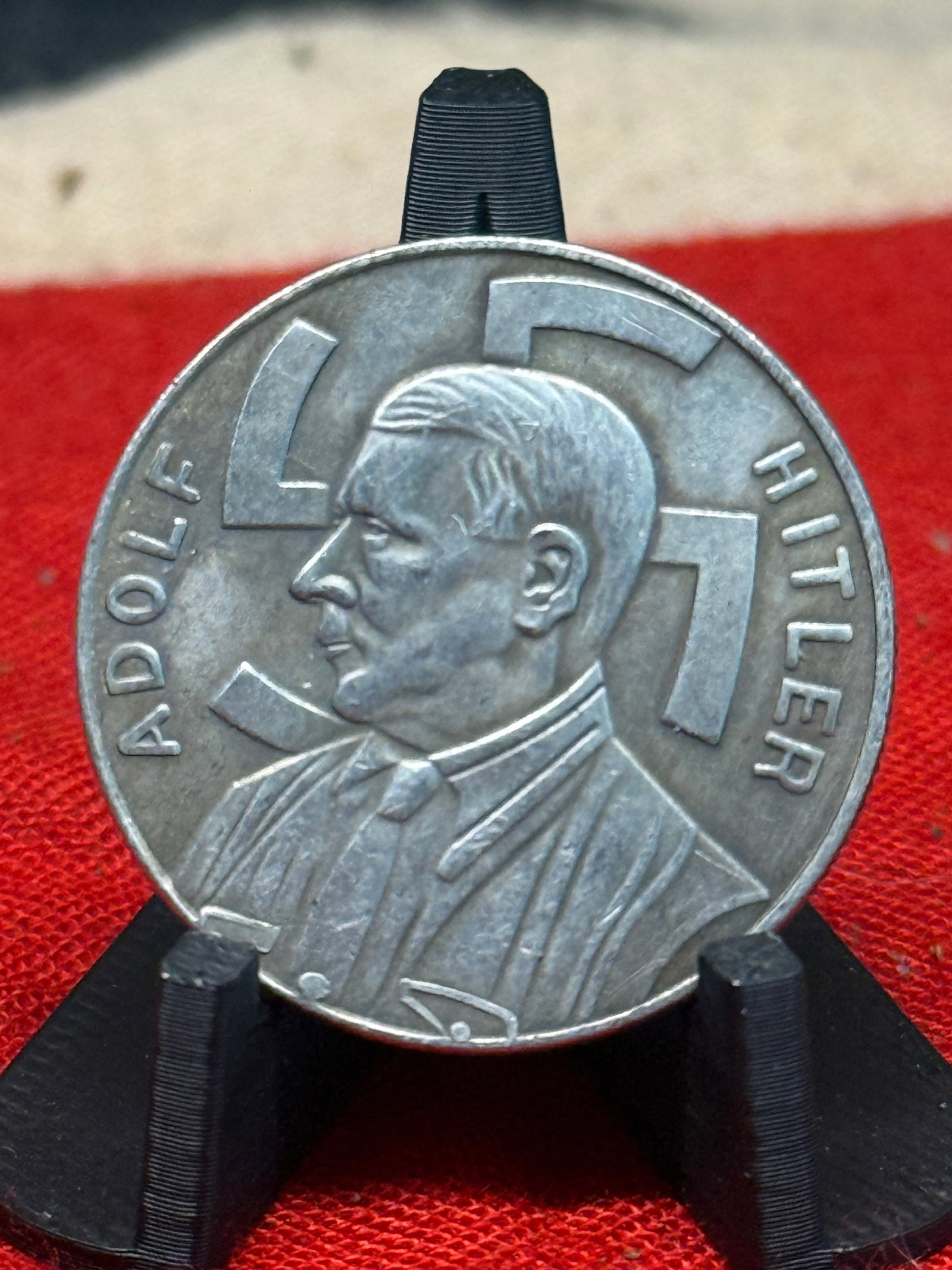 WWII German Adolf Hitler “1 Reichsmark?? Spende Donation Token: This circular silver-gray German token presents a prominent left-facing portrait of Adolf Hitler, accompanied by his name “ADOLF HITLER” around the perimeter and a large swastika positioned be