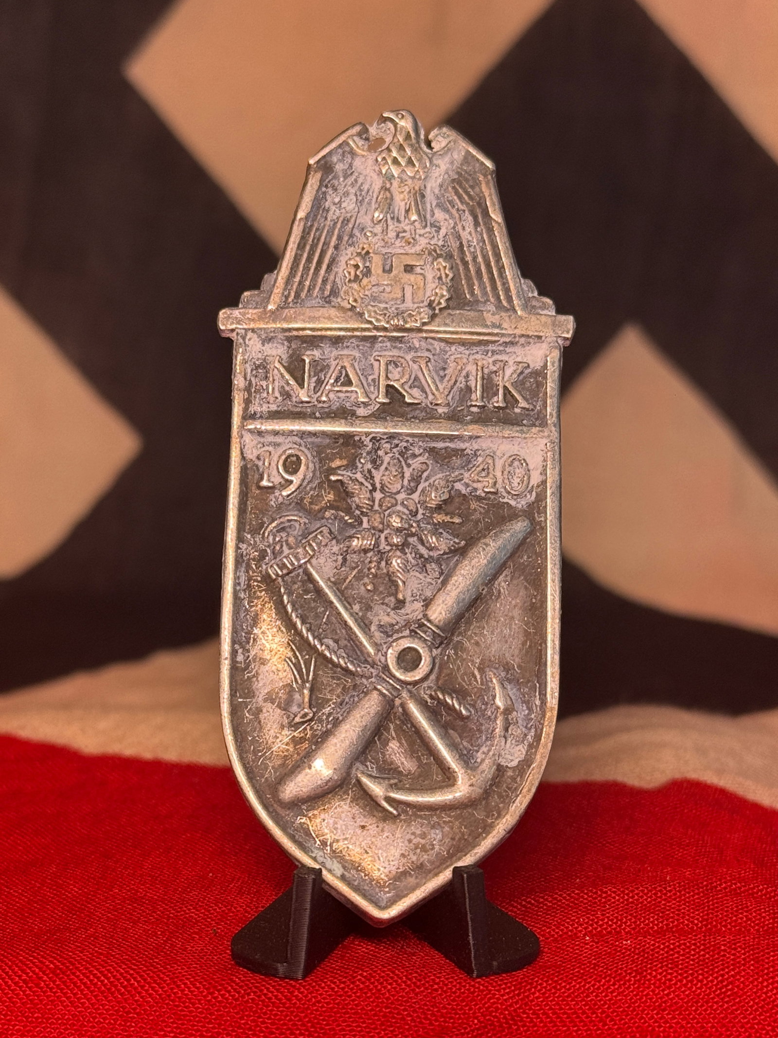 WWII German Kriegsmarine Narvik 1940 Campaign Shield Badge: A substantial metal shield-form badge bearing the inscription “NARVIK” above the divided date “19 40,” surmounted by a German national eagle and wreathed swastika. The lower field inco