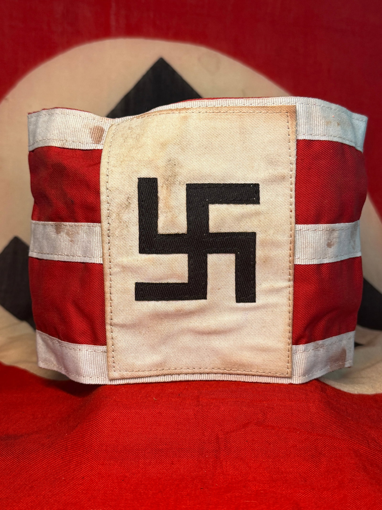 WWII German NSDAP Political Leader Swastika Armband with White Stripes: A visually distinctive WWII German armband constructed from red fabric with three horizontal white textile bands and a large rectangular off-white central panel bearing a sewn black swastika. Unlike t