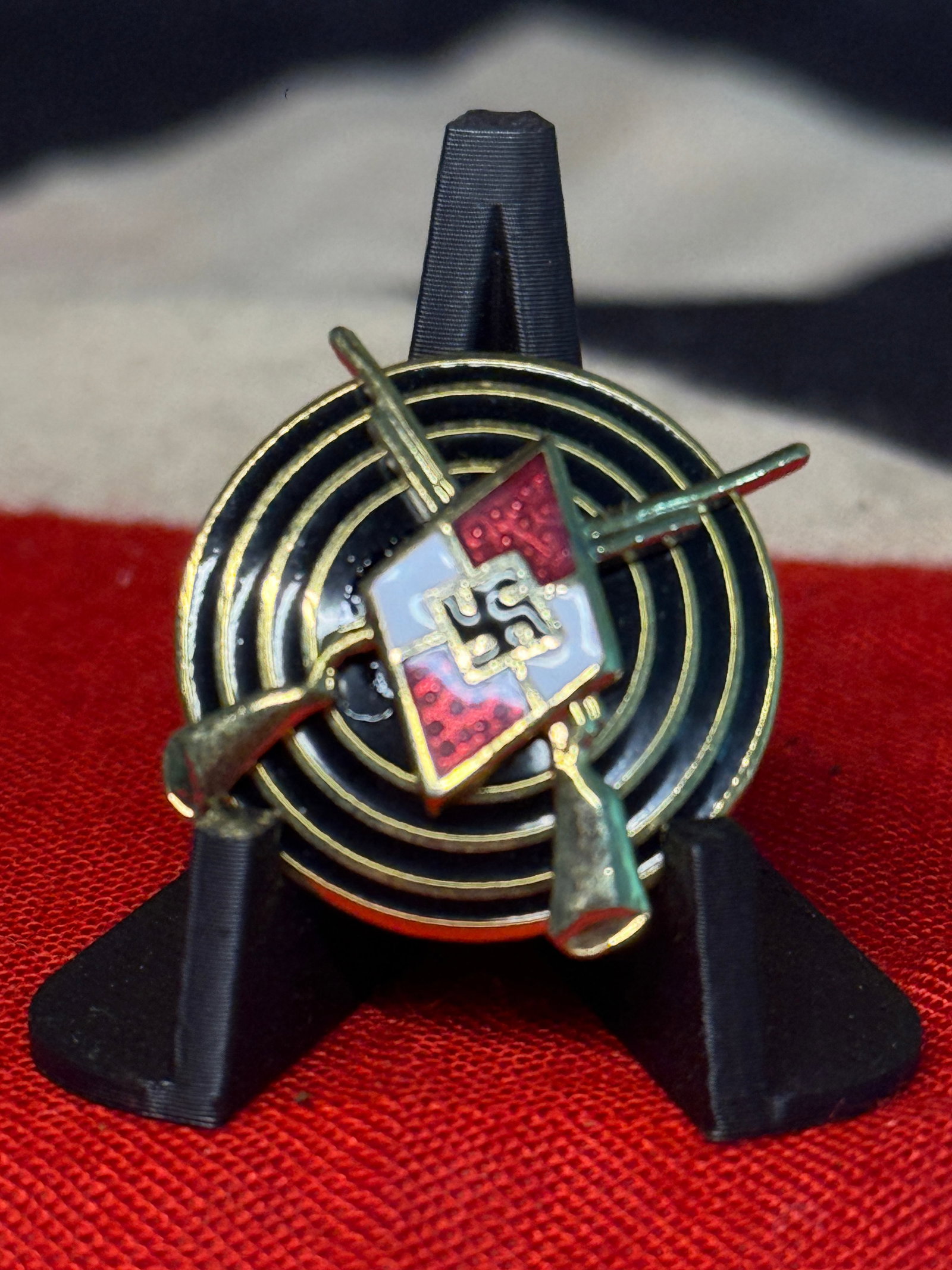 WWII German Hitler Youth Shooting Marksman Badge – RZM M1/123 Marked: A distinctive circular German Hitler Youth shooting award featuring a black enameled target composed of concentric rings, overlaid by crossed rifles and the red-and-white diamond-shaped Hitler Youth e
