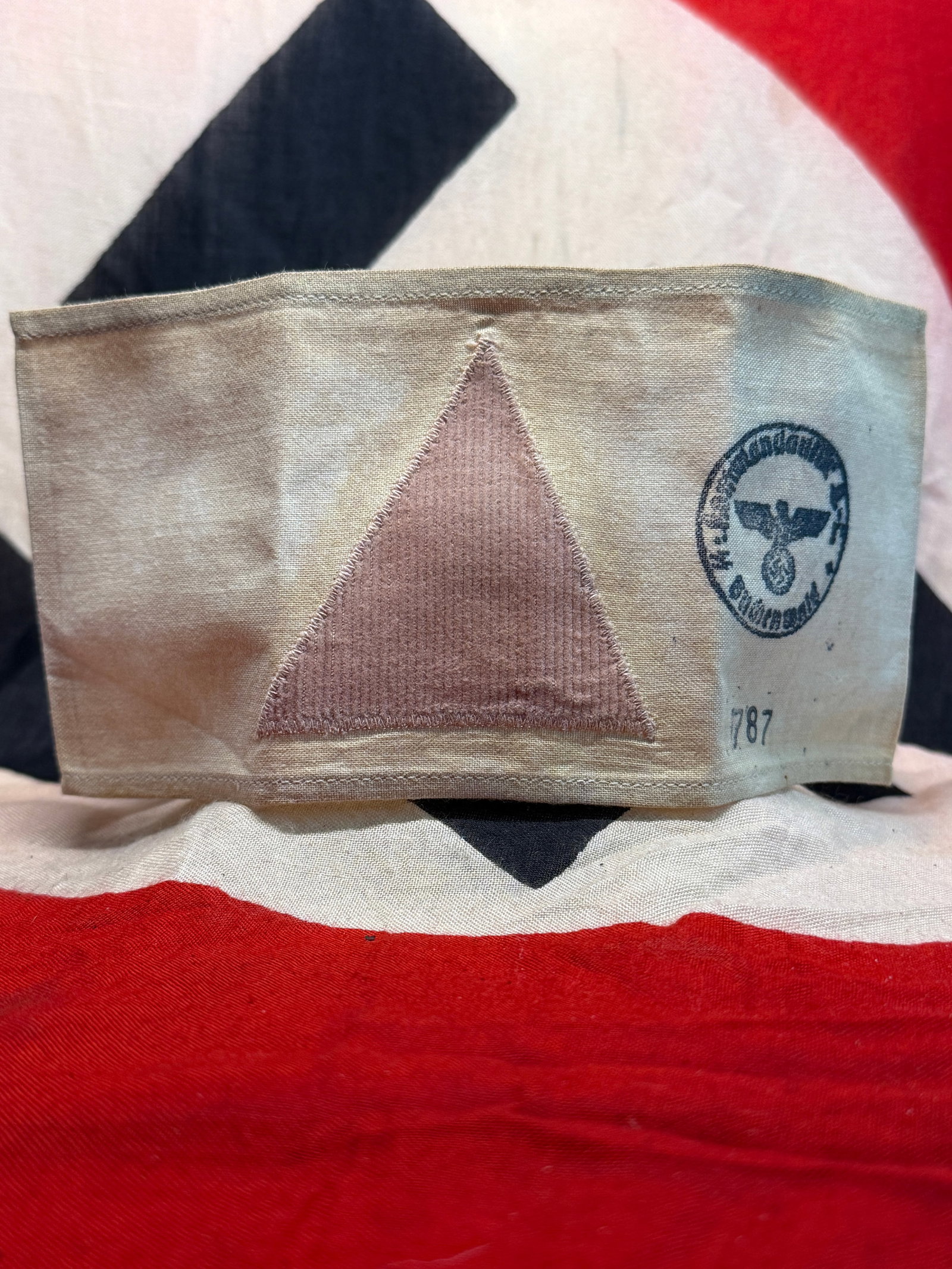 WWII German Concentration Camp Prisoner Identification Armband with Pink Triangle & Camp: A stark textile identification armband constructed from light-colored cloth and fitted with a centrally sewn pink triangular patch. The pink triangle was among the prisoner-classification symbols empl