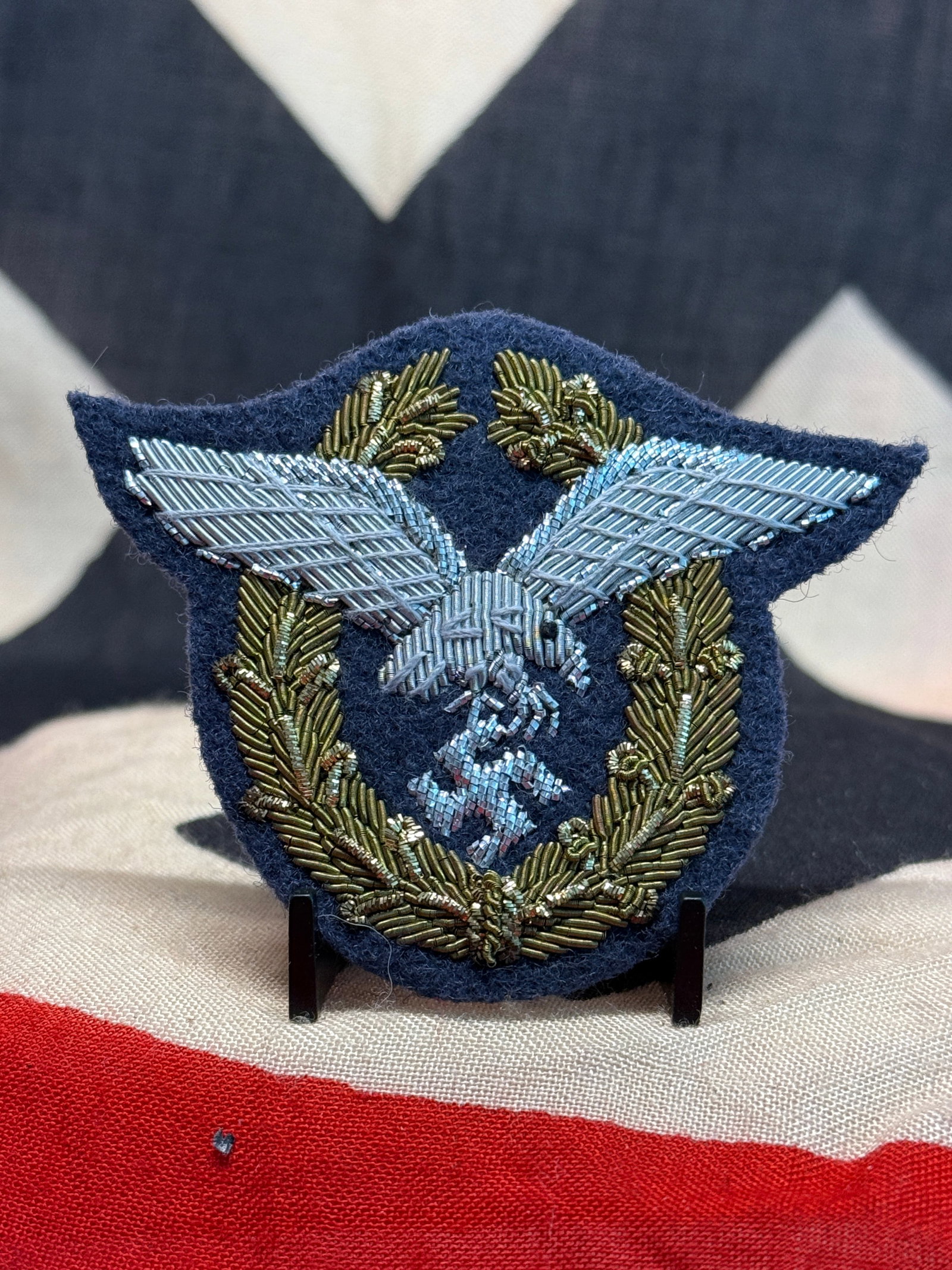 WWII German Luftwaffe Officer Bullion Eagle & Wreath Uniform Insignia: An elaborate hand-embroidered Luftwaffe uniform insignia worked in metallic bullion on a dark blue wool backing. Dominating the center is a large silver bullion Luftwaffe eagle with extended wings and